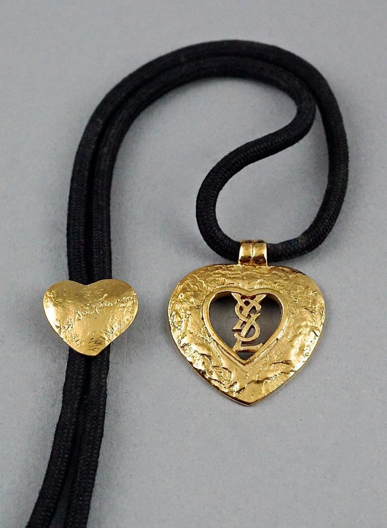 Vintage YVES SAINT LAURENT Ysl Monogram Heart Lariat Necklace

Measurements:
Height: 1.88 inches (4.8 cm)
Adjustable Cord: 21.65 inches (55 cm) maximum

Features:
- 100% Authentic YVES SAINT LAURENT.
- Textured heart pendant with YSL monogram.
-