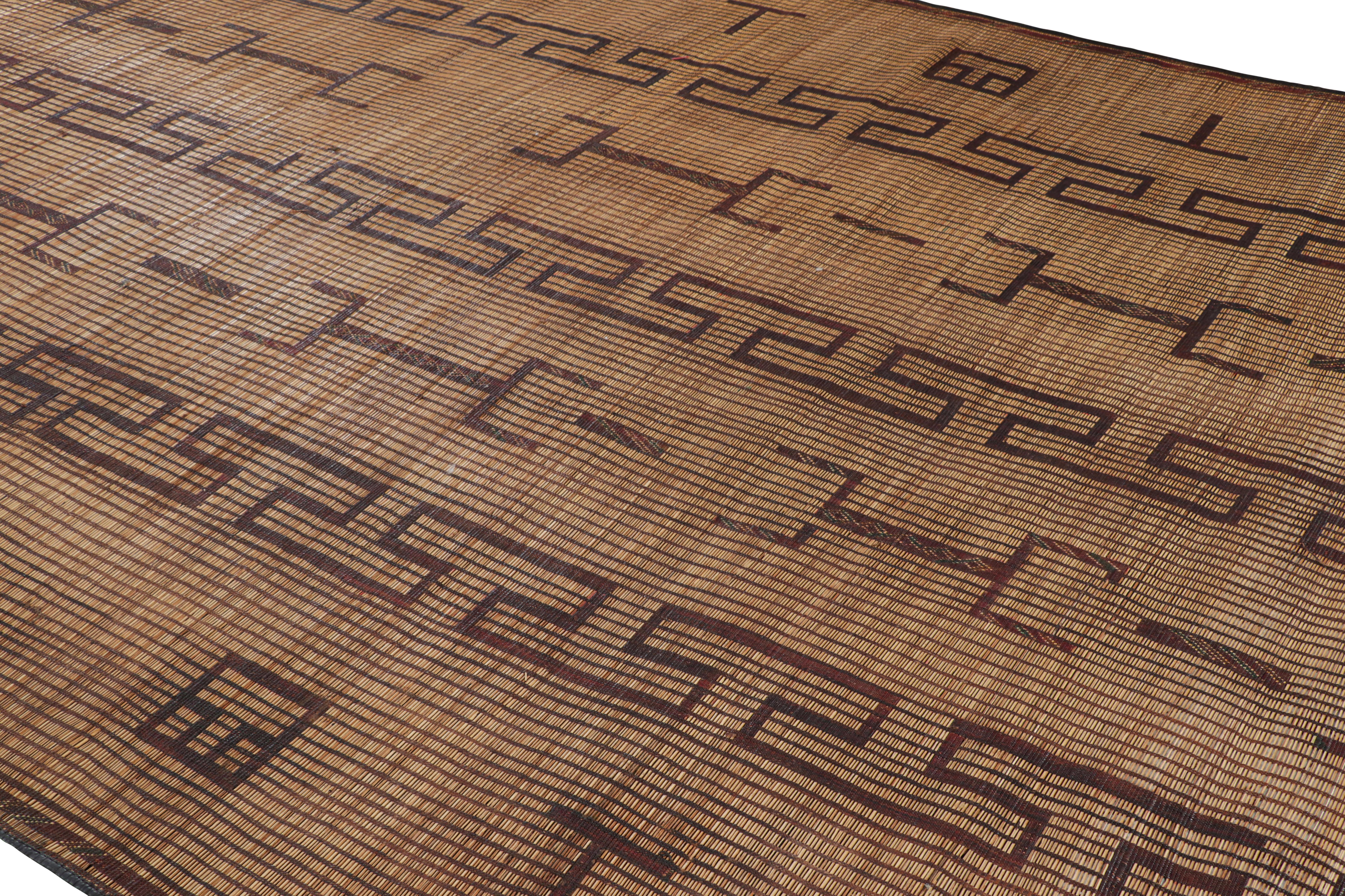 This vintage Moroccan floor covering is a 9×16 Tuareg mat from the nomadic tribe of the same name. Handwoven with reeds and leather circa 1950-1960, its natural materials enjoy warm beige, brown and black tones in its geometric patterns.

On the