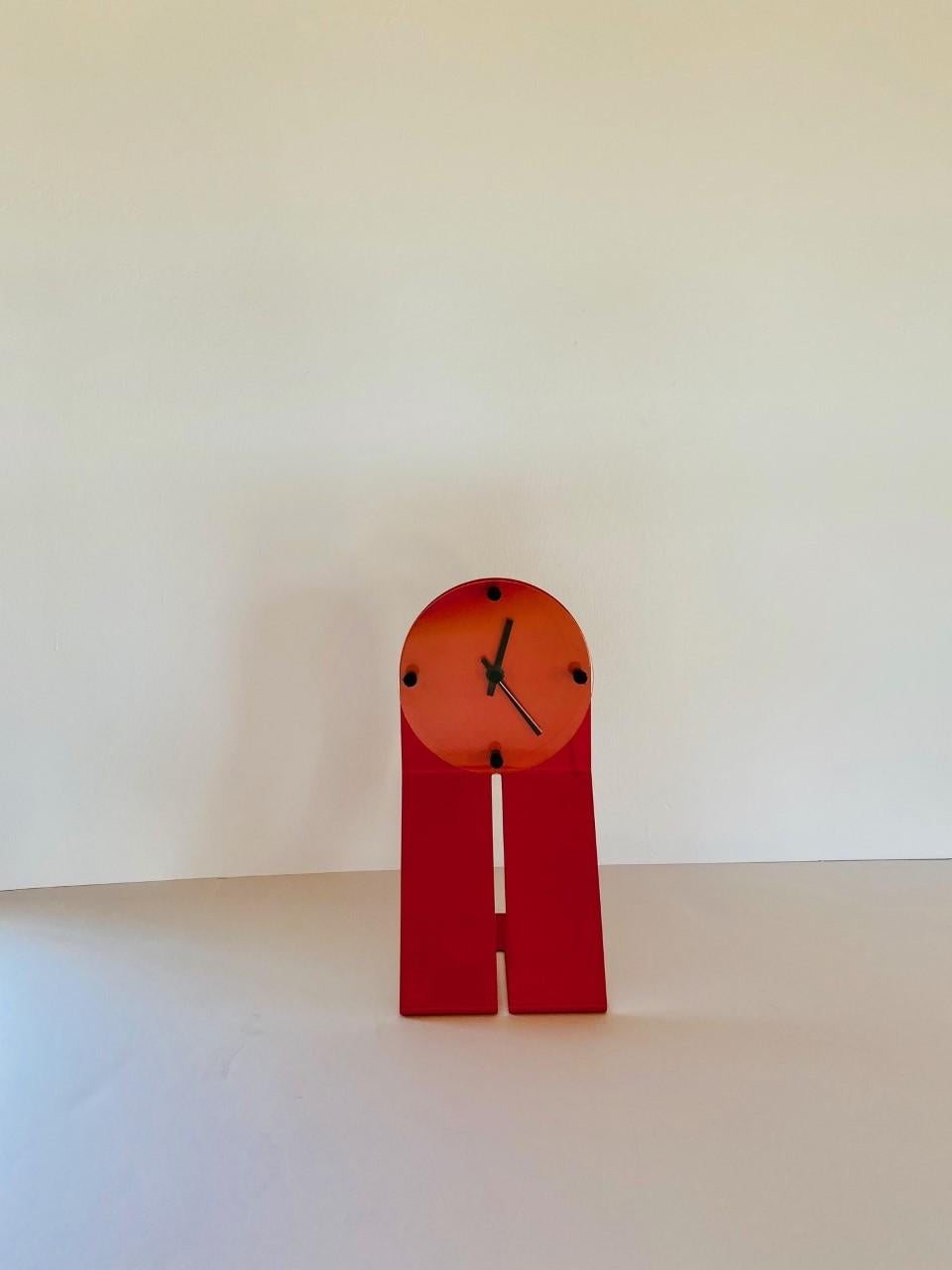 Graphic and high design piece by Seccose. The metal frame is bent to create an effect on profile. The piece is powered coated in a unique orange red color, finished with a plexiglass circle that protects the quartz time mechanism. This piece was