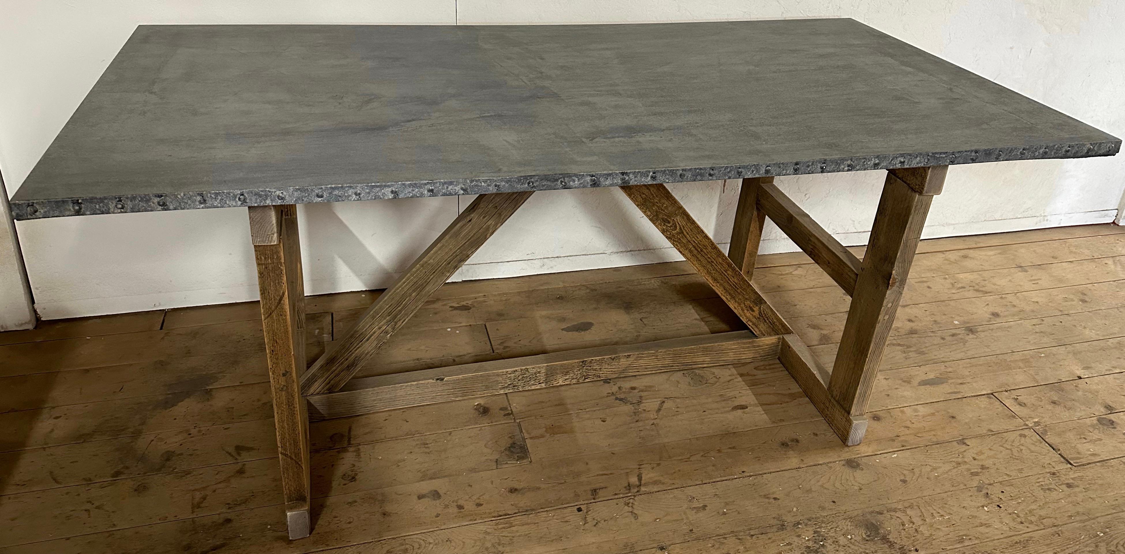 Cette table de ferme, de cuisine ou de jardin de style français vintage en zinc repose sur une base à tréteaux de style industriel. La base des tréteaux en chêne vieilli et le plateau bien oxydé donnent à cette table de ferme une superbe patine et