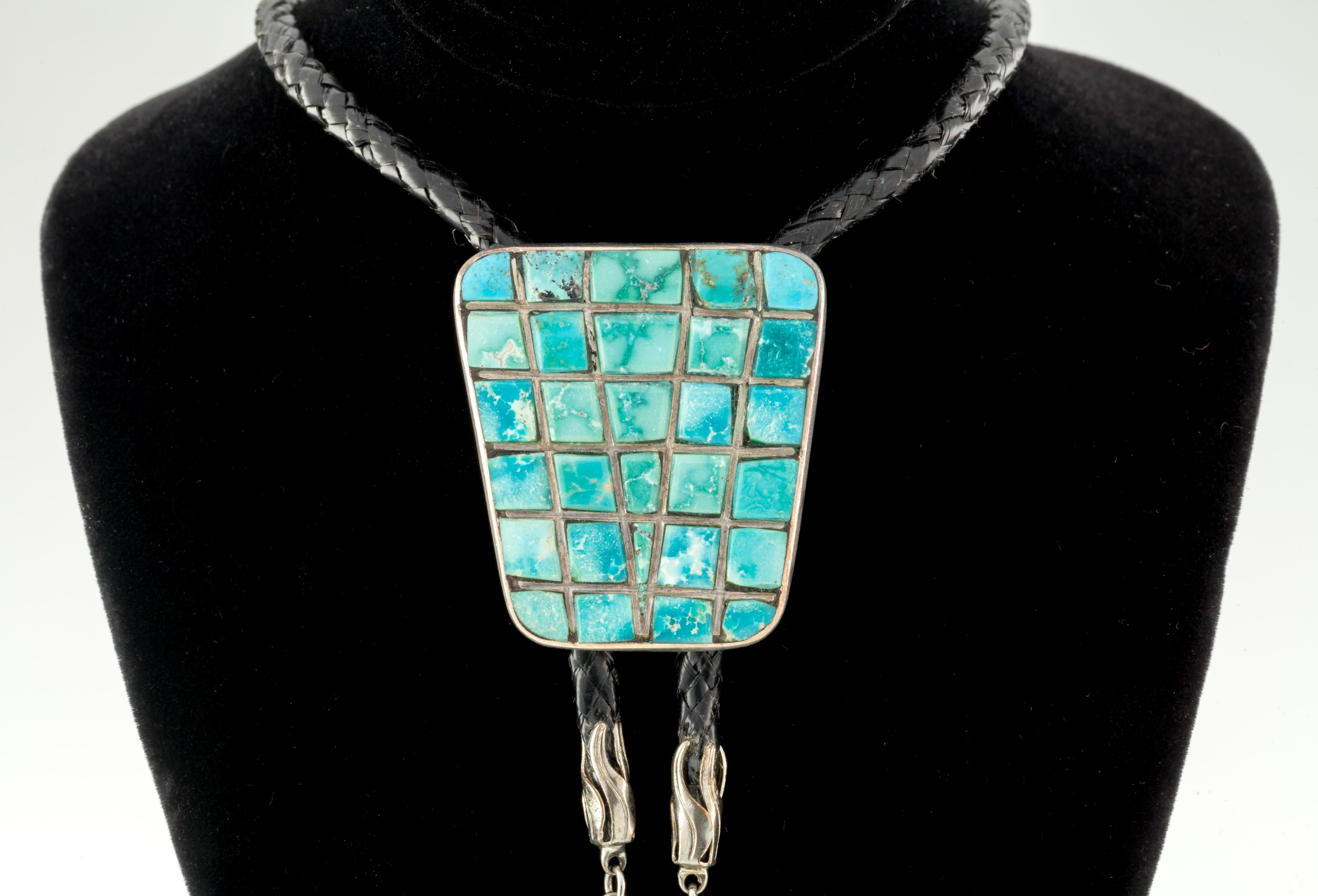 Beautiful Turquoise Inlay Bolo with Black Leather tie accented in Sterling and more Turquoise  
Natural Inlay stones set in tapered figure   
Length & Width of Bolo = 41 mm X 37 mm
Total Mass w/leather = 35.2 grams
Beautiful Hand-Crafted Piece 