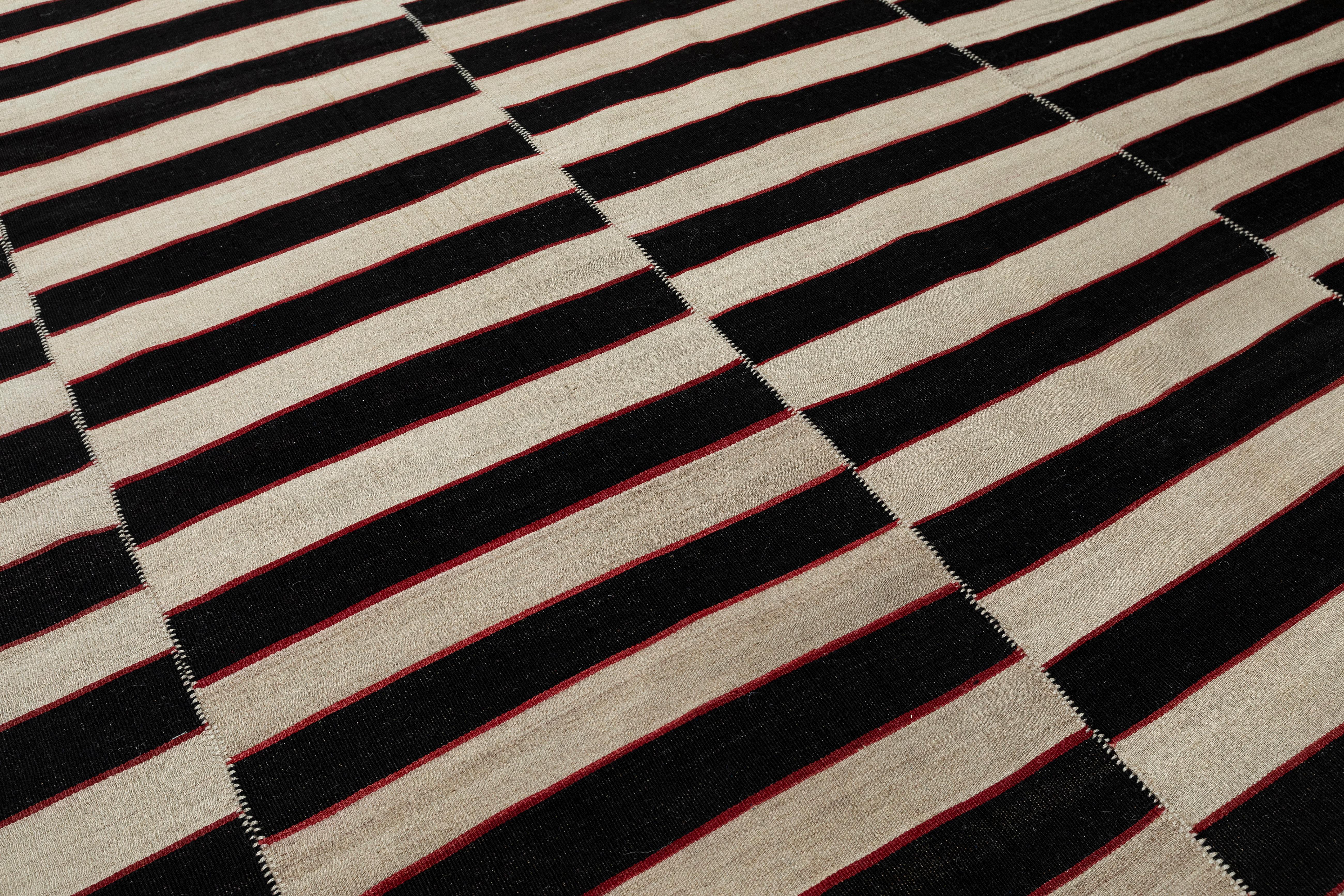 This Vintage Persian flat weave rug is crafted from hand-spun wool and dyed with natural vegetable pigments, offering a striking black-and-white striped design with subtle red accents. Its bold, minimalist pattern blends traditional craftsmanship