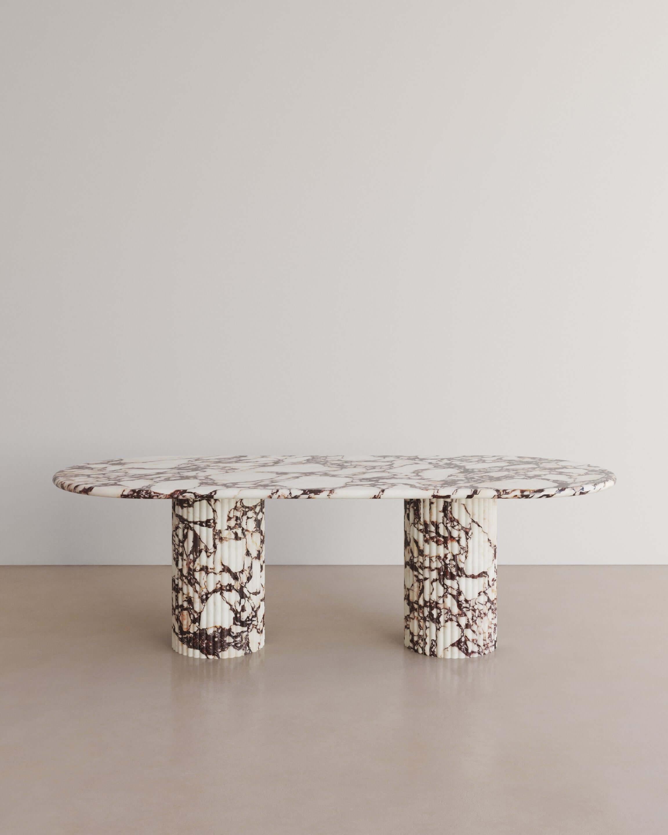 The Essentialist brings you The Antica Dining Table II in Calacatta Viola Marble. An oval table top resolved by smooth bullnose edges rests on two supporting pillars. Architectural form is refined by artistic expression echoing Roman culture. This