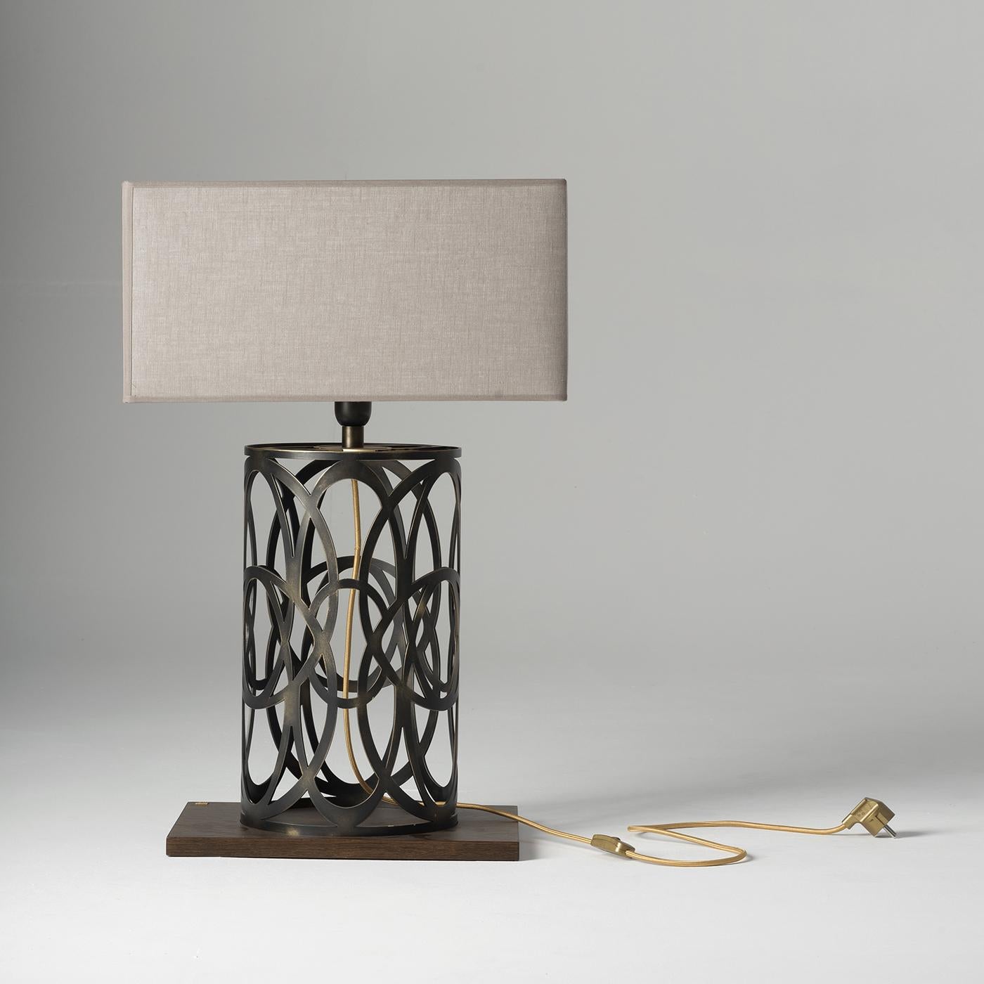 The Violante table lamp is defined by a geometric base, boasting an intricate cage-like structure crafted from acid-etched brass. Finished with a wooden support and a refined fabric shade, this lamp makes a stylish addition to any table, cabinet or