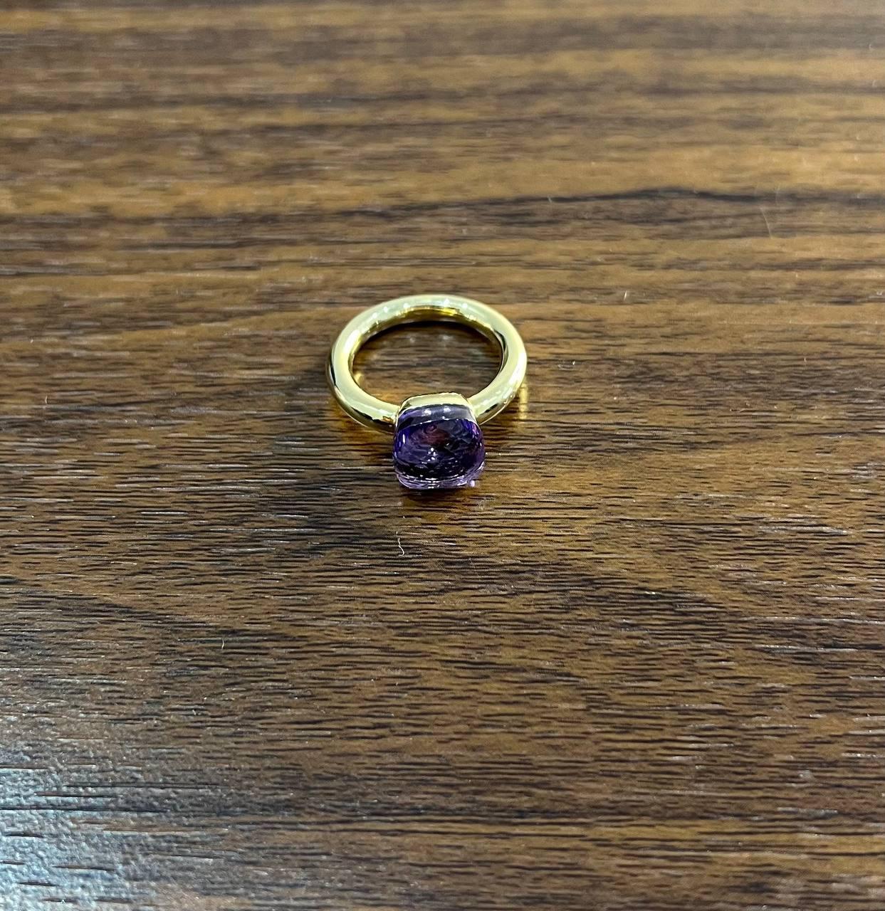 A striking ring featuring a cushion-cut purple amethyst set in a sleek gold band. The gemstone's smooth, polished surface catches the light beautifully. The band is simple yet elegant, complementing the stone's vibrant hue. 14K Yellow Gold.