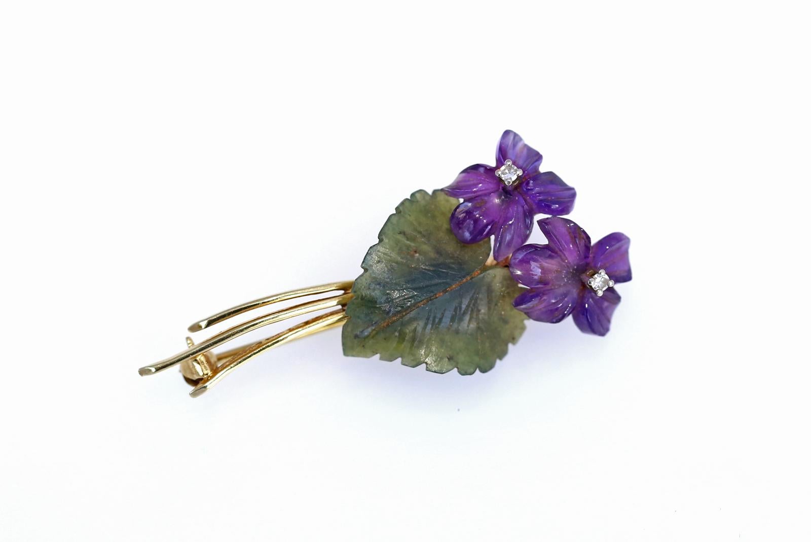 Violet flowers brooch comprising: Amethyst, Jade (jadeite) and Diamonds.
Yellow gold 585/000 (14K)
A pair of engraved amethyst flowers with a green leaf made of jadeite. In the centre of the flower, there are two fine white Diamonds. Handcrafted by