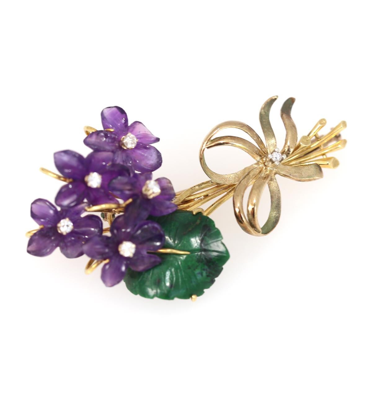 Violet flowers brooch comprising: Amethyst, Jade (jadeite) and Diamonds.
Yellow gold Stamped LIV 18K. 
Five engraved amethyst flowers with a green leaf made of jadeite. In the centre of the flower, there are fine tiny white Diamonds. 
Once it was