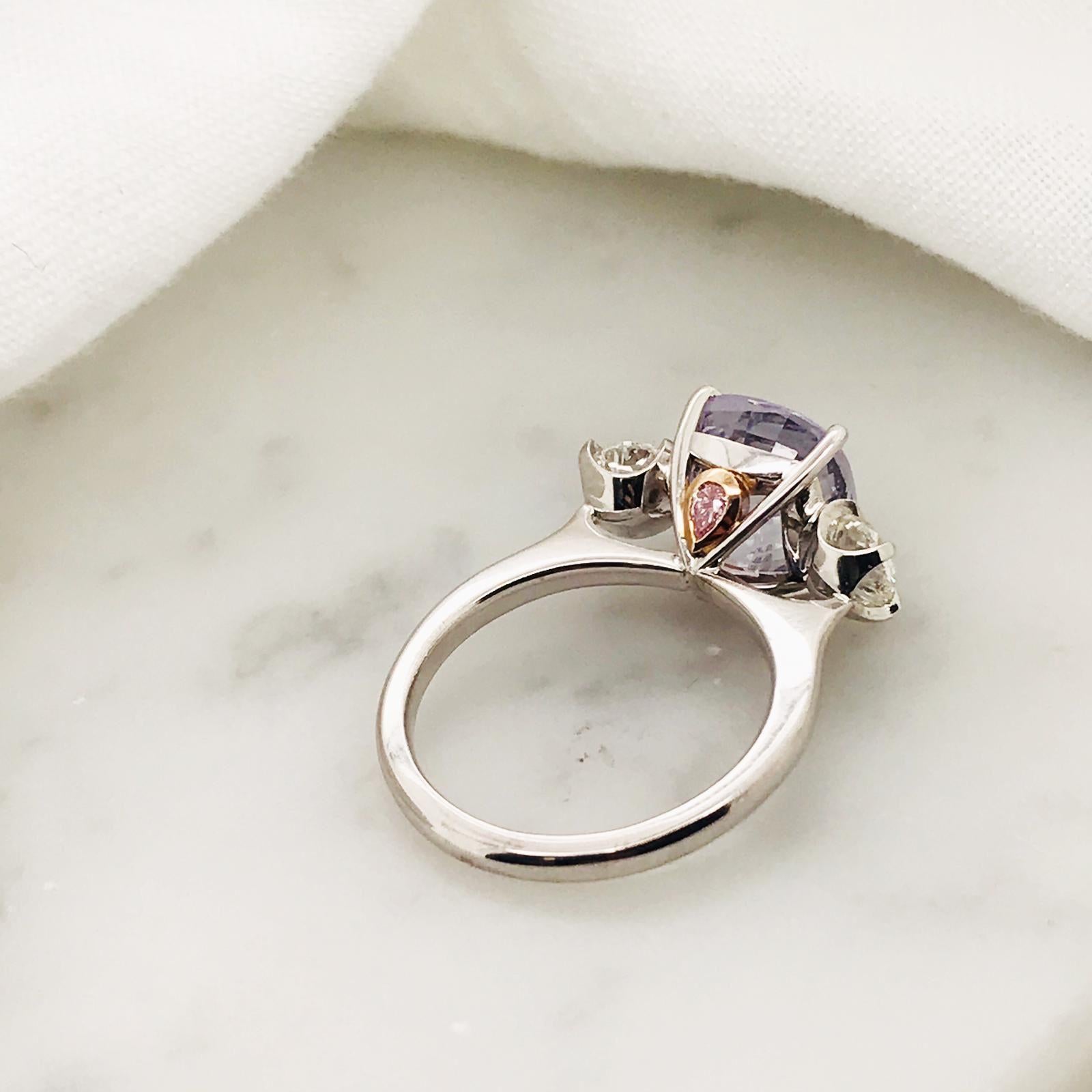 Trilogie-Ring aus 18 Karat Weißgold und 18 Karat Roségold

Der Mittelstein ist ein atemberaubender violetter Ceylon-Saphir im Kissenschliff von 5,32 Karat (unbehandelt), flankiert von zwei Diamanten im Altminenschliff 

2 x versteckter Pink Argyle