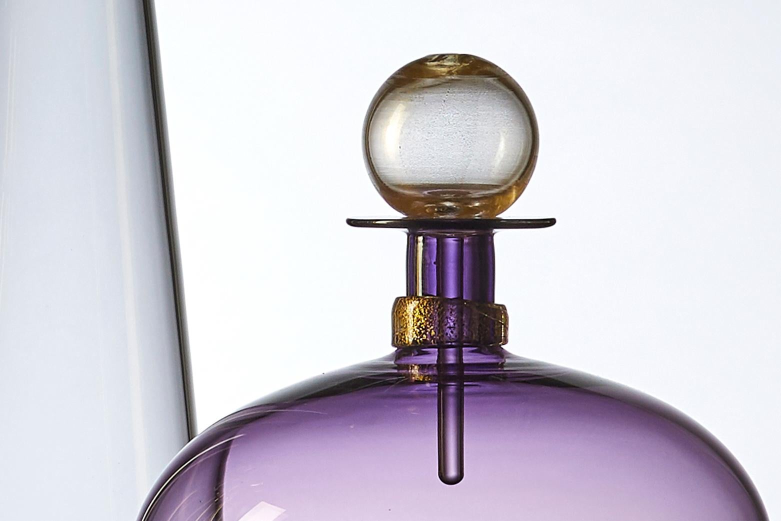 The modernist hand blown Jewel Bottle by Vetro Vero features tinted violet glass, and shimmering gold details. Inspired by apothecary collections and decanters of Mid-Century Modern design, the light purple carafe makes a standalone statement or a