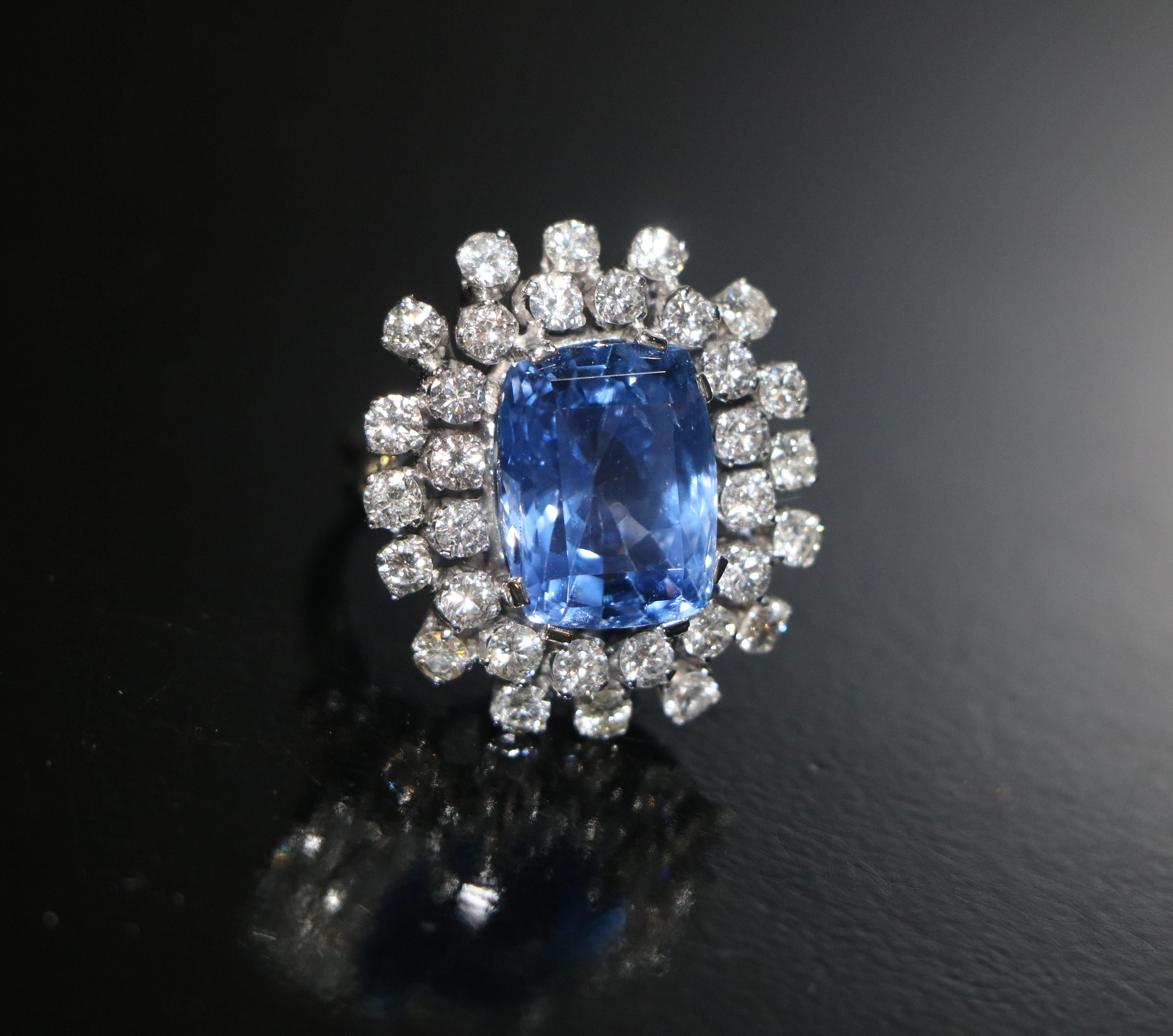 Platinring, besetzt mit natürlichen Diamanten (insgesamt 4,65 Karat) und einem Saphir von 18,30 Karat.
Es handelt sich um einen Saphir (Varietät des Korunds) von violettblauer Farbe, geschliffen in einem rechteckigen Kissen, Kompositschliff. Er