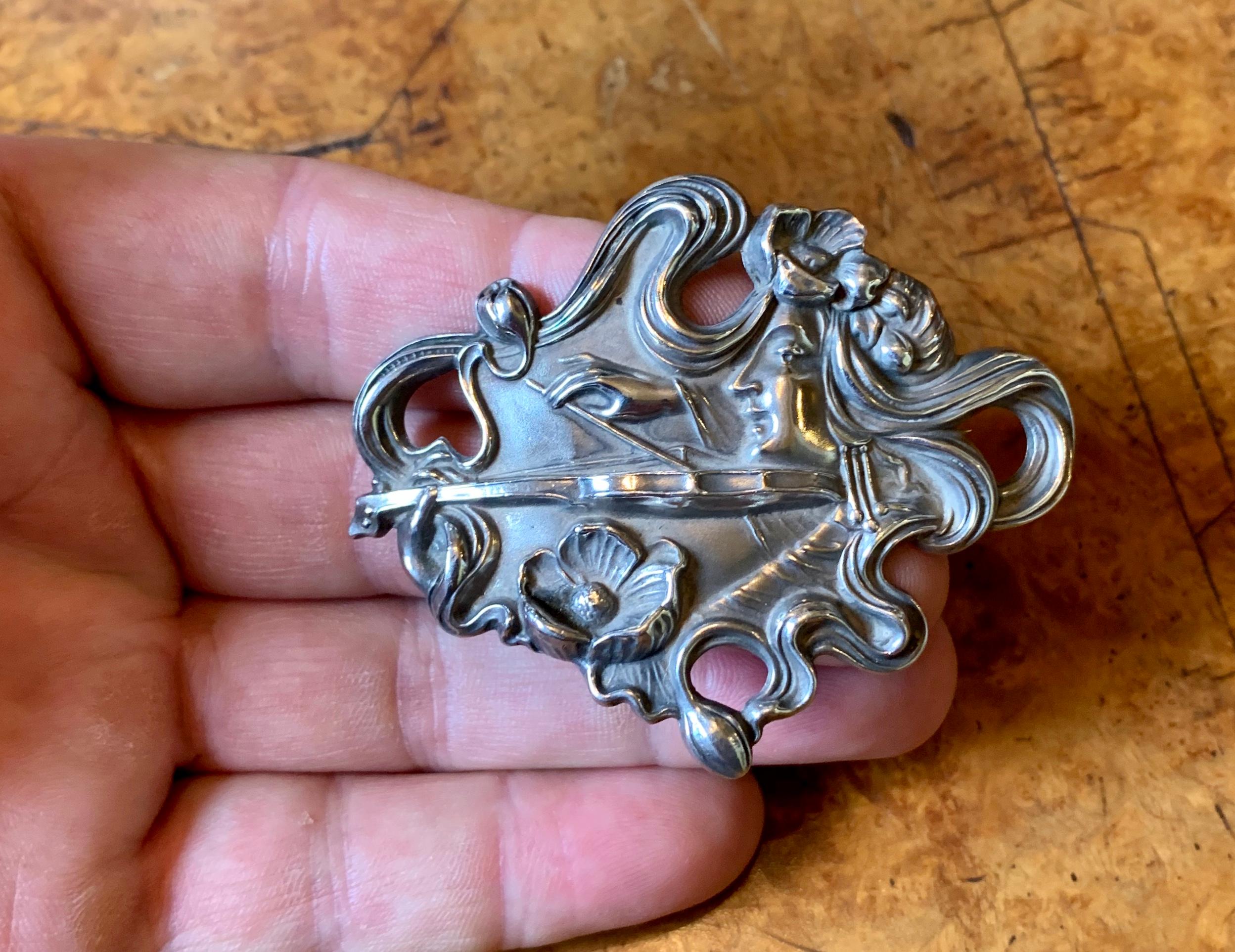 This is a museum quality Art Nouveau Brooch in Sterling Silver depicting a woman musician playing a violin or viola. This rare and extraordinary motif is rendered with exquisite Art Nouveau beauty.  The musician bows her violin while her hair, which