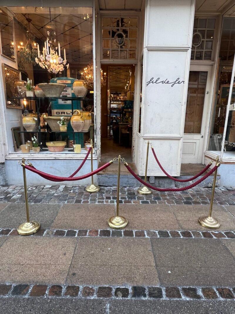 Elegant barrage de contrôle de foule VIP du milieu du siècle, composé de 5 poteaux en laiton avec deux crochets chacun, ainsi que de trois cordes rouges en velours, d'une corde recouverte de cuir et d'une corde plus longue en velours vert, que vous
