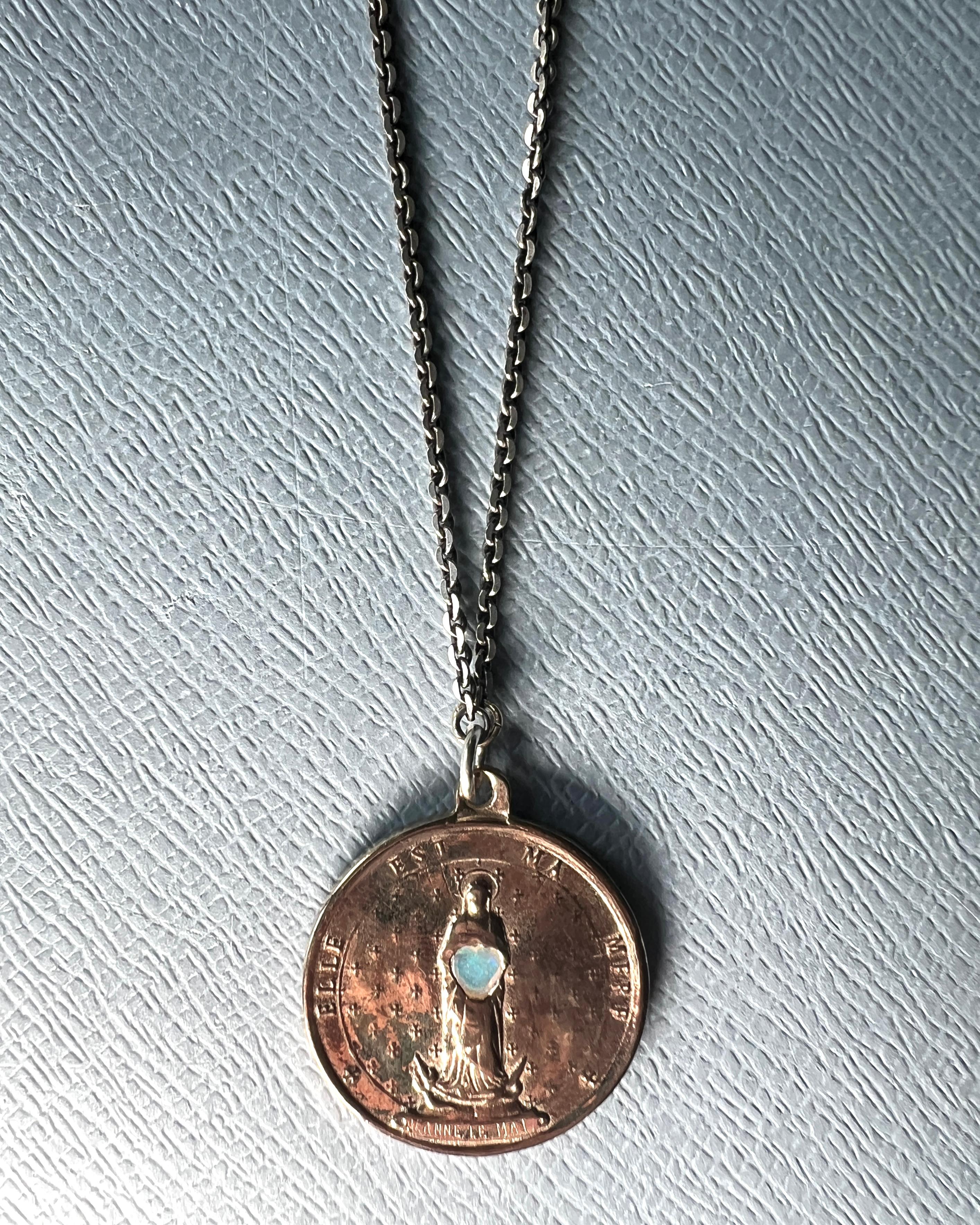 Heart Opal set in the middle of this French Miraculous Medal in Bronze hanging on a Silver Chain Necklace.
Protection Amulet

Length: 29.5 inches

Designer: J DAUPHIN 

Jeanne le mat – She Is My Mother
This round French medal, inscribed with “Jeanne