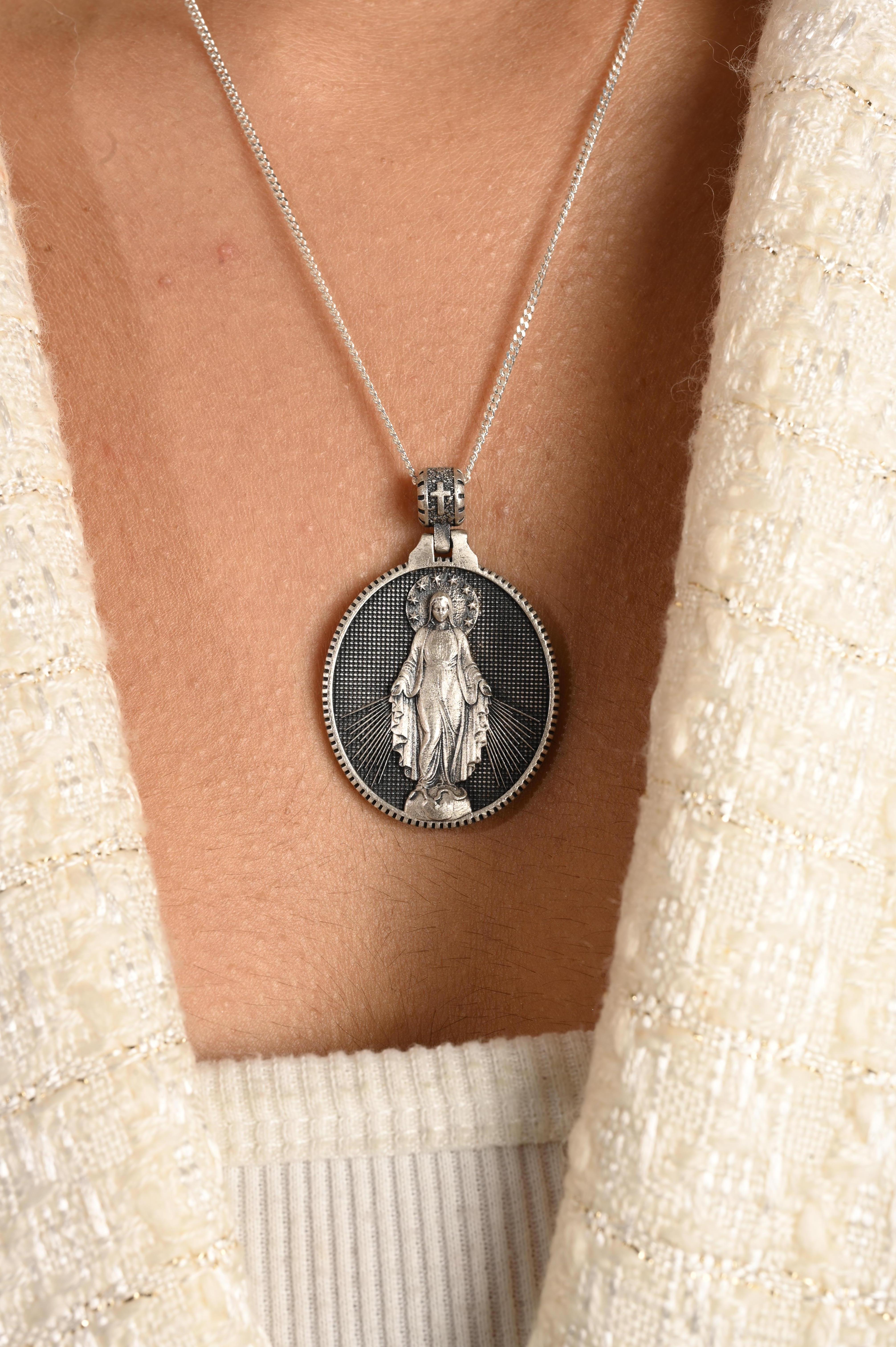 Dieser doppelseitige Medaillon-Anhänger der wundertätigen Jungfrau Maria ist ein kraftvolles Symbol des Glaubens und des Schutzes. Auf der einen Seite ist das Bild der Jungfrau Maria zu sehen, die als wundertätige Mutter Gnade und Barmherzigkeit