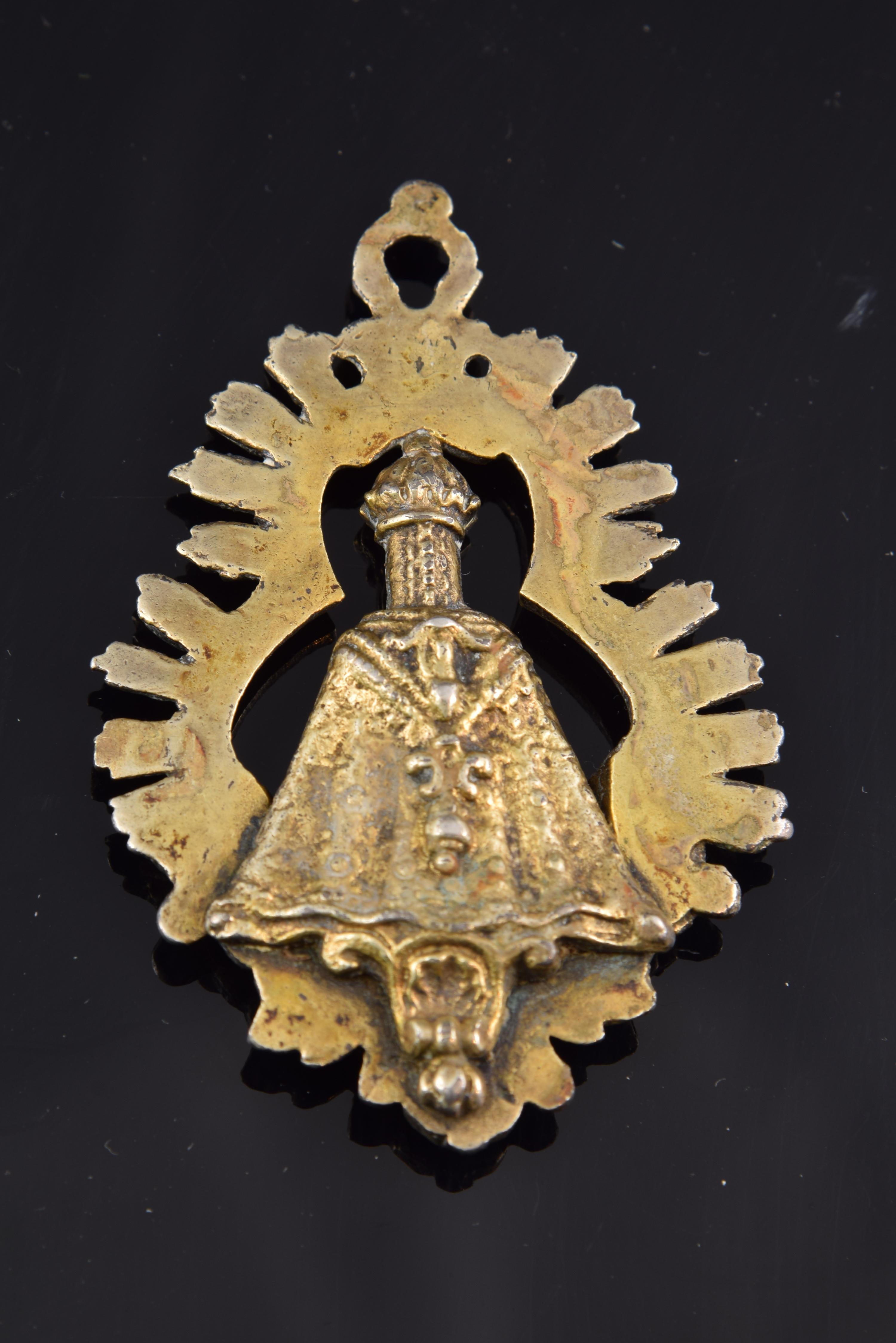 Medaille. Spanien, 18. Jahrhundert.
 Andachtsmedaille aus vergoldetem Metall, die ein Bild der Jungfrau Maria zeigt, das auf einem Sockel steht und von einem strahlenden dreilappigen Heiligenschein umgeben ist. Im unteren Bereich sind Köpfe von