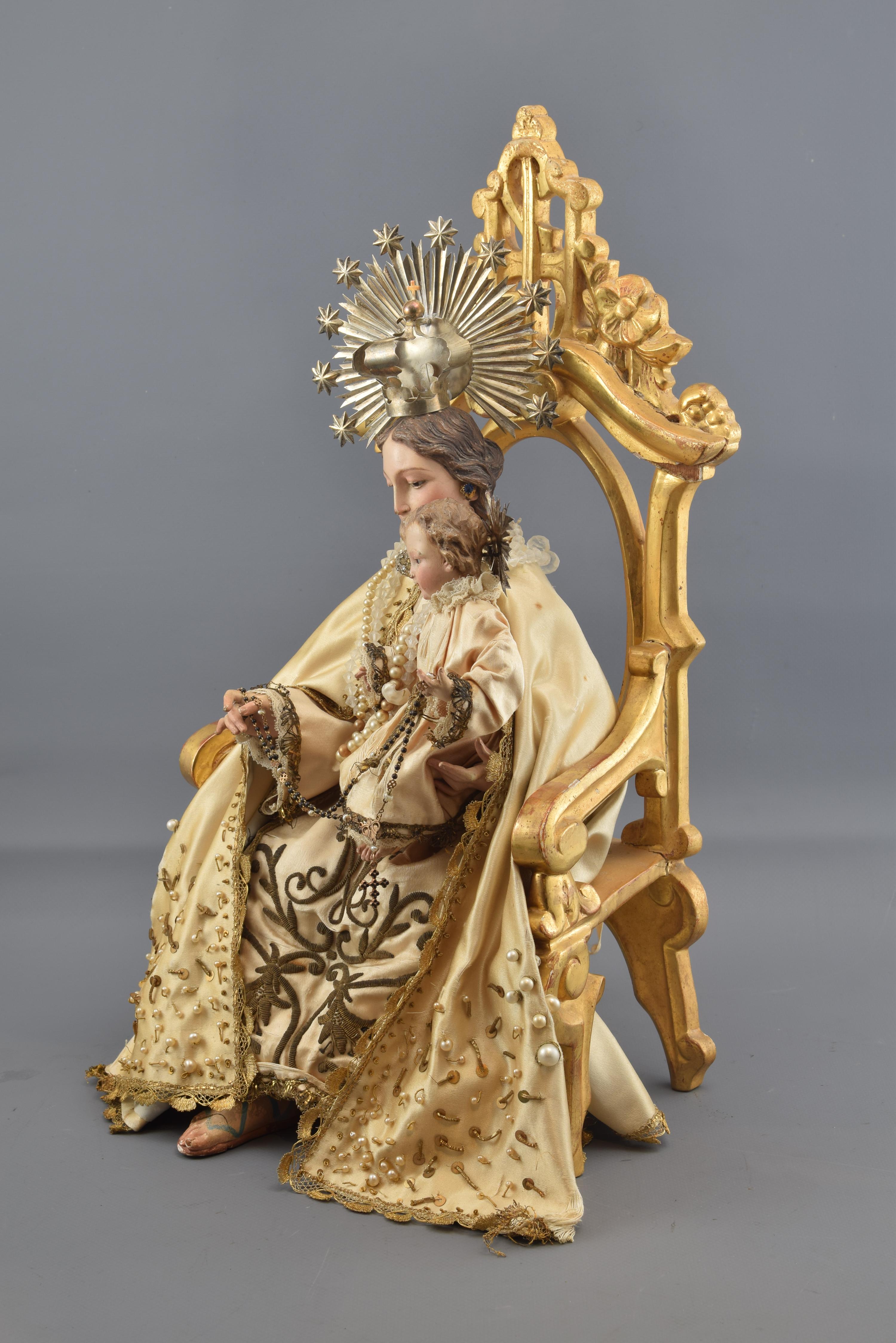 Virgin with Child Jesus (with dresses) on a throne. Wood, metal, textile, etc. Spain, 19th century.
Virgin crowned dresser sitting on a throne of carved and gilded wood decorated with plant and architectural elements and with the Baby Jesus, also