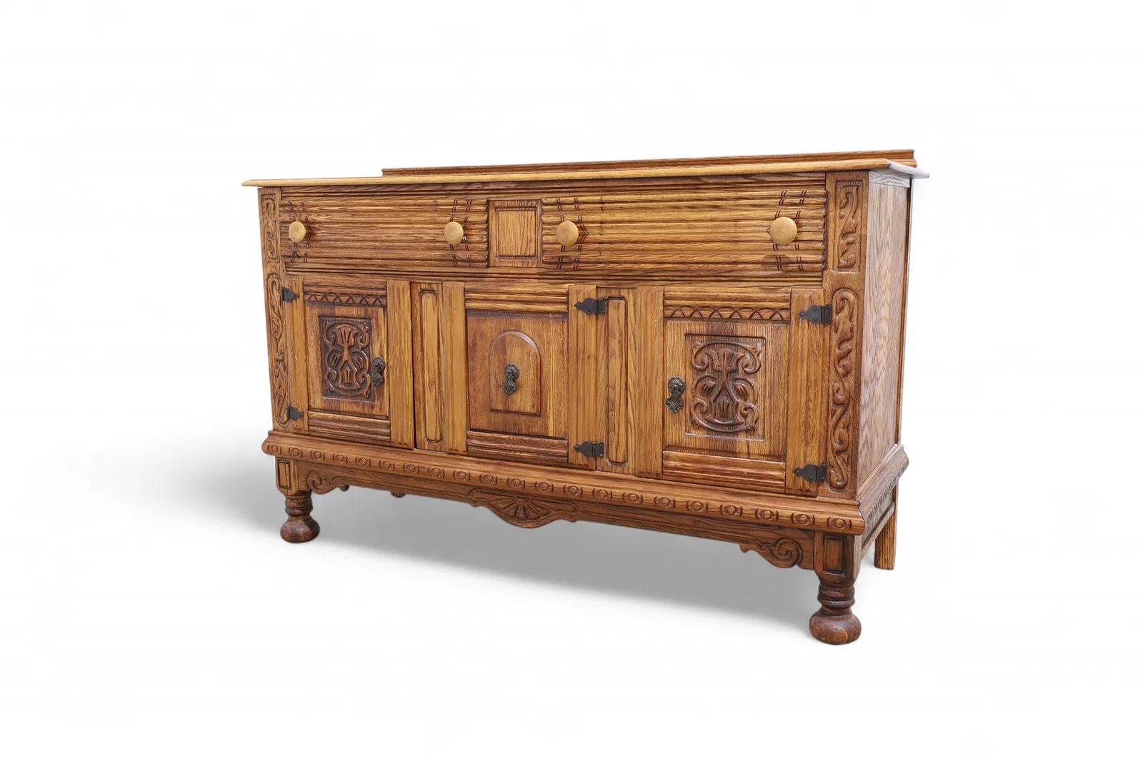 Credenza in rovere intagliato di Virginia House, con pannelli frontali dettagliati e ferramenta classica in ferro. Il pezzo presenta un mobile centrale affiancato da due ante laterali con intagli decorativi, sopra un lungo cassetto superiore. Un