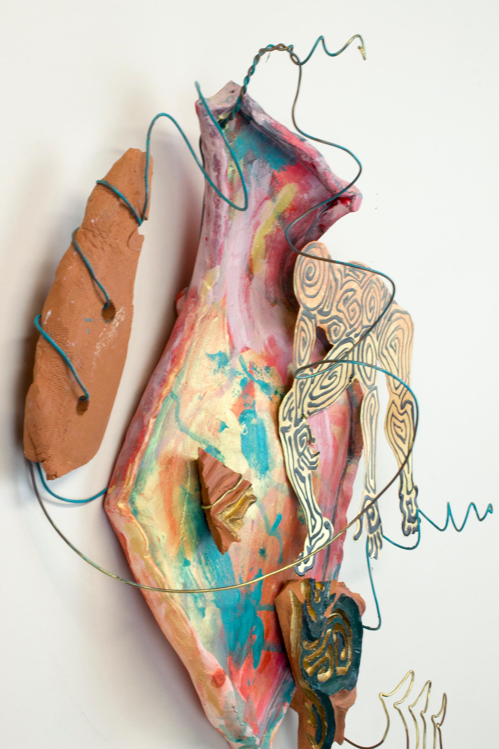 Virginia Mahoney’s “Illogical Sequence” is an 18 x 14 x 7 inch ceramic and metal wall sculpture in peach, teal, pink, gold, green, and brown. A cutout metal figure painted in gold and black reaches for a ceramic shard on a painted ceramic