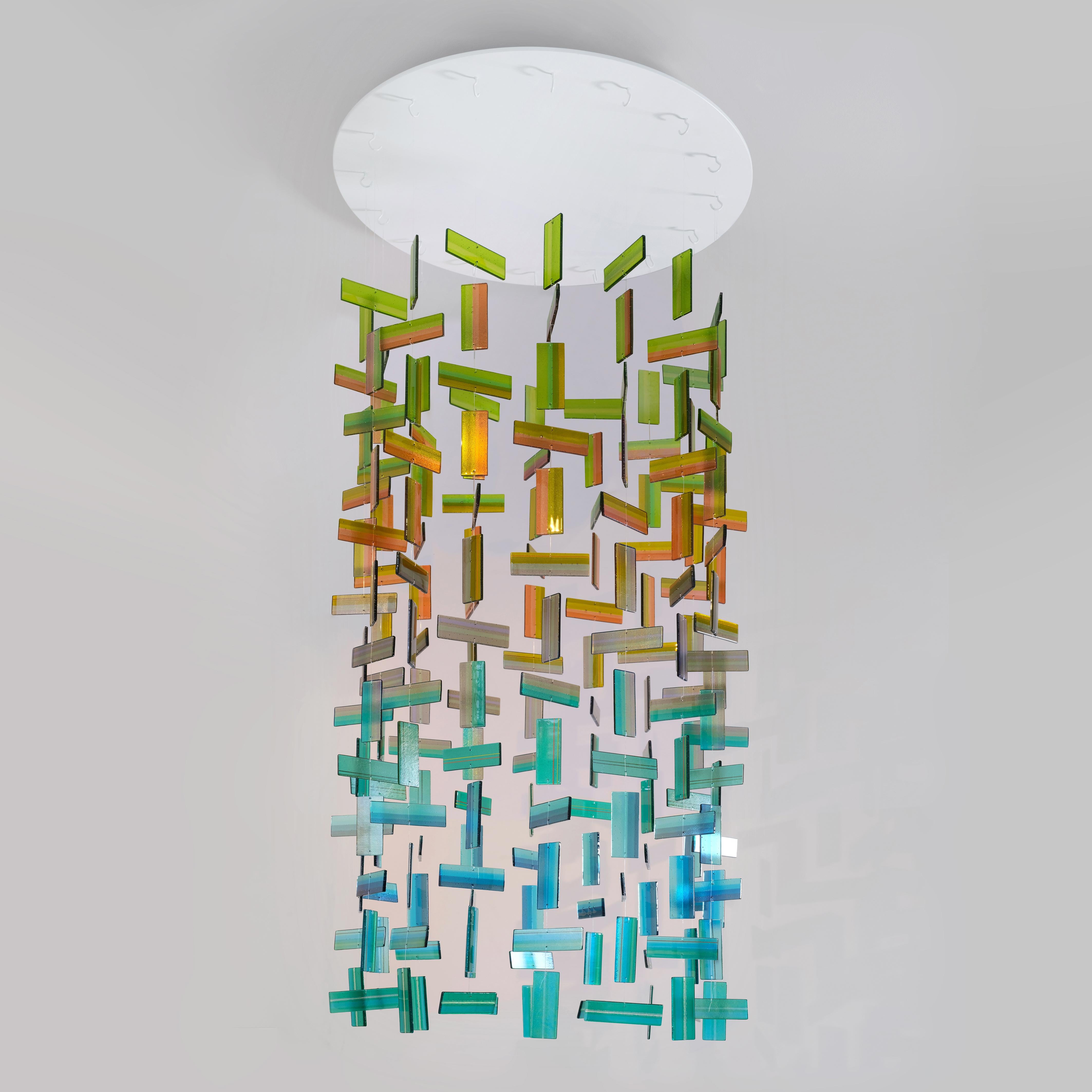 Viridian est une sculpture suspendue unique en verre fusionné vert, ambre et aqua, réalisée à la main par l'artiste britannique Amy Cushing. Une installation suspendue à couper le souffle, composée d'une multitude d'éléments en verre fusionné