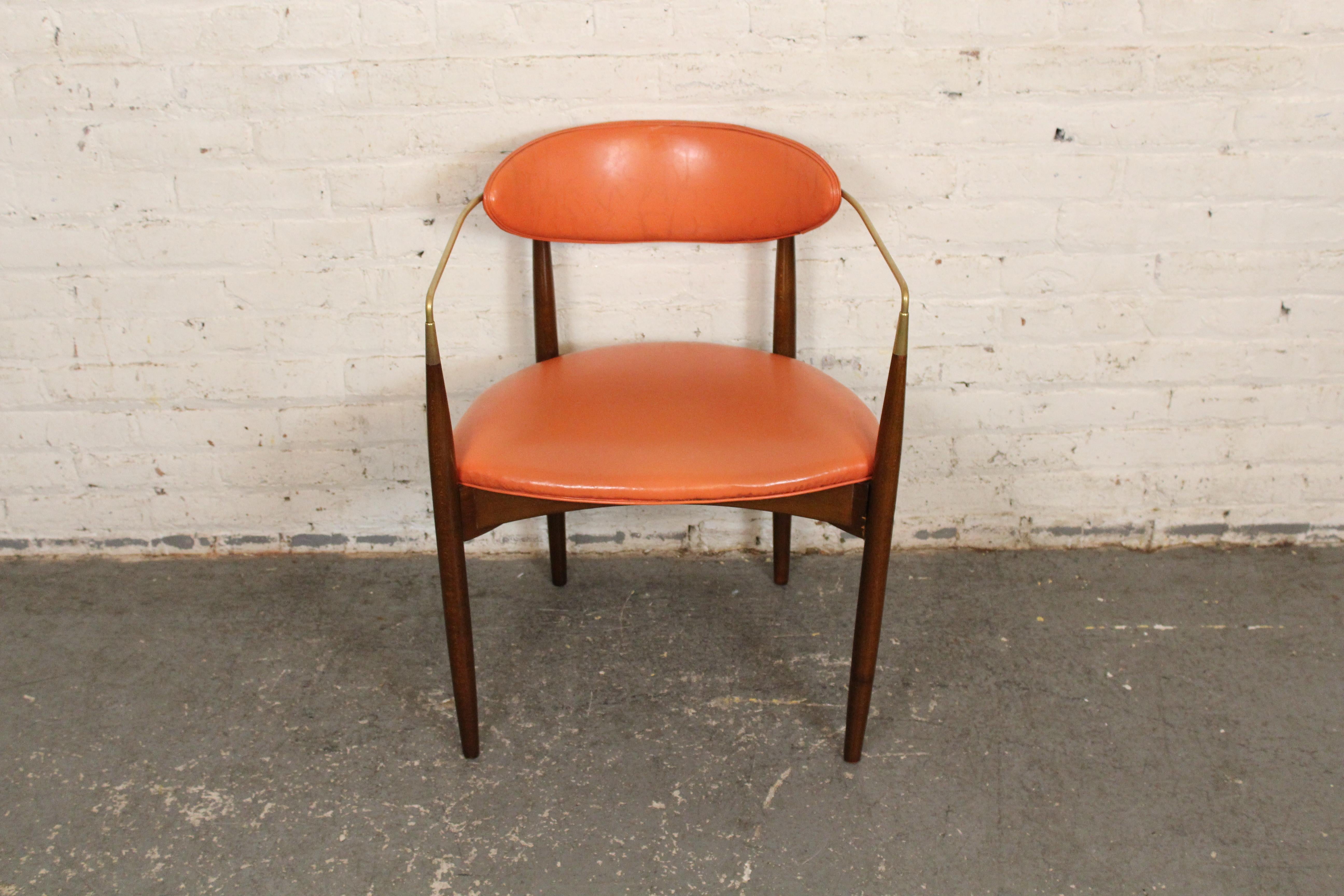 This arm chair was made in the 1950s and still feels modern today. With a thin polished brass arm that wraps around the back rest, and connects to a walnut frame. The seats are  original orange vinyl.
Please confirm location with vendor NY or NJ