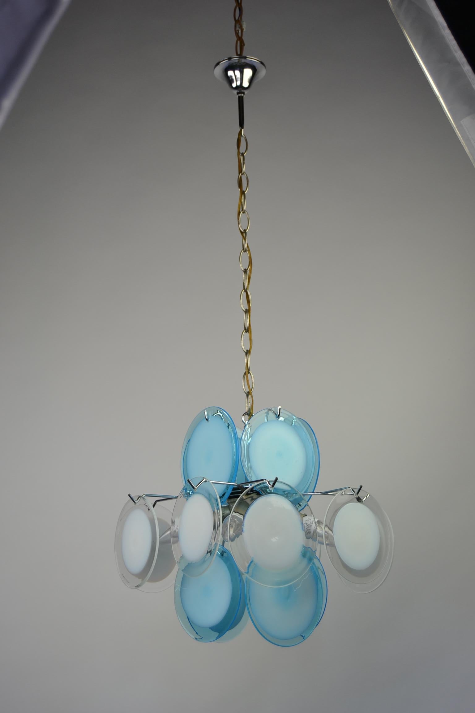 Mid-20th century Vistosi chandelier - Vistosi pendant.
The chrome base has 16 glass Murano discs in the colors blue and white with 4 light points E14 fitting. 
This Italian Lighting dates 1960-1970 and is in good used condition. 
1 glass disc has