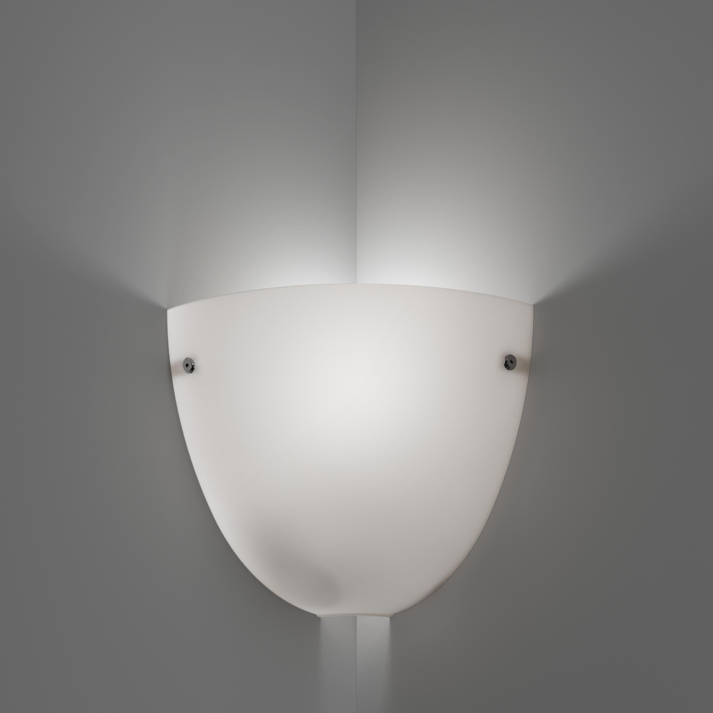 The Corner sconce in satin blown glass has an intuitive shape that adapts to every corne, helping create an intimimate ambient light, ideal for a bedroom. Glass color tone in satin white. Metal parts in white. E26 lighting.
