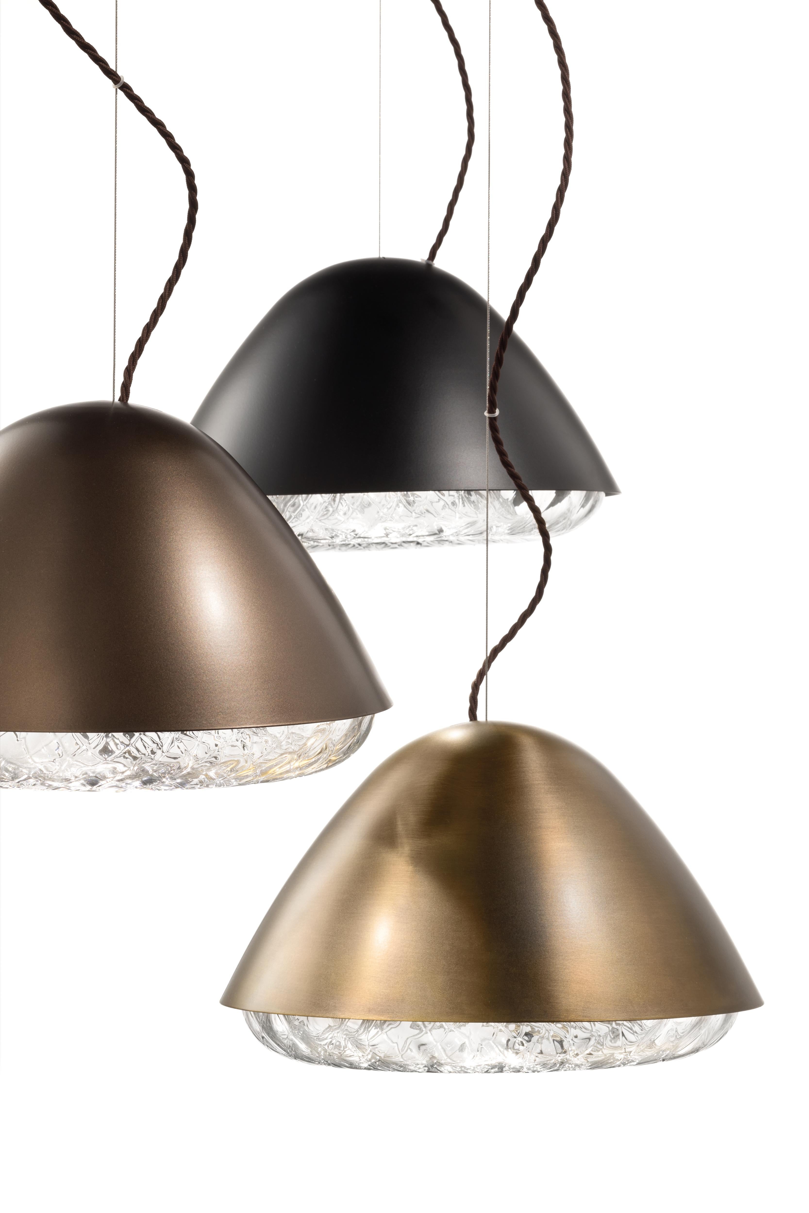 Kira is a collection of lamps combining metal with blown glass. The result is a set of lighting systems composed of two antithetical halves: a diffuser in crystal glass, decorated and embellished with a rich surface texture, topped with a turned