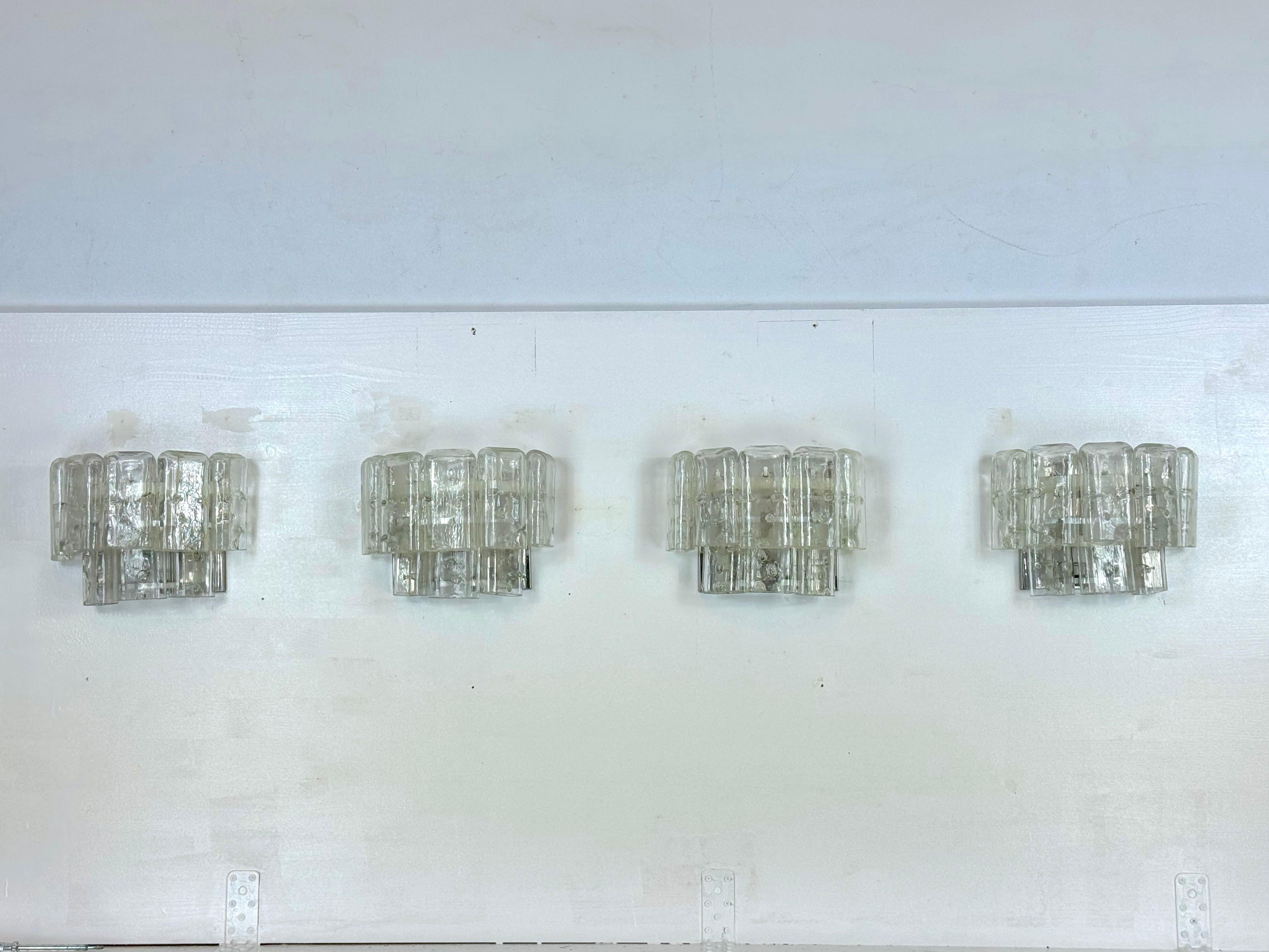 Set di quattro lampade da parete con elementi in vetro di Murano trasparente prodotte in Italia negli anni '70. Attribuibile a Vistosi. Nessuna etichetta o marchio. Ottime condizioni vintage senza scheggiature o crepe, staffe in metallo con normali