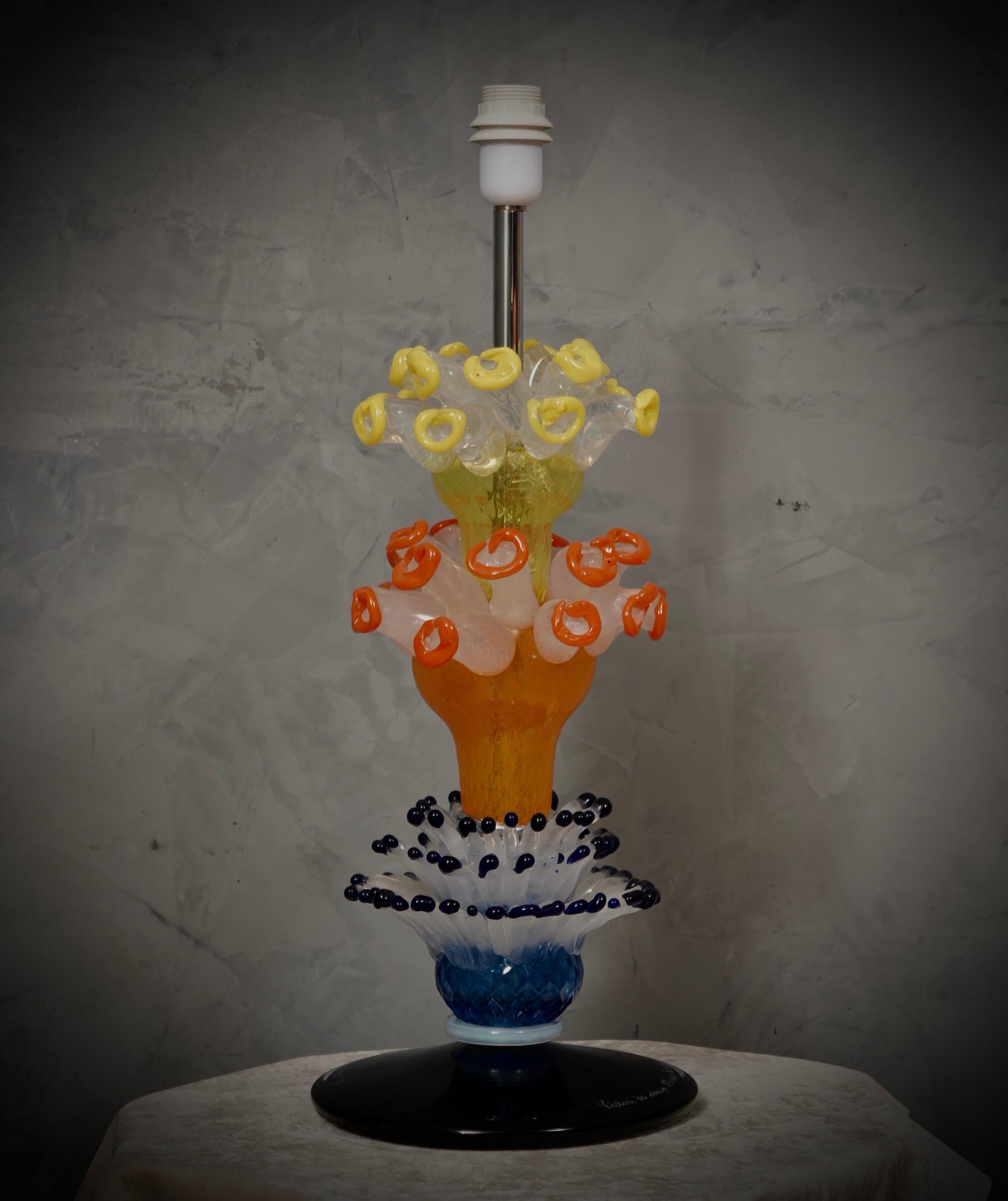 Lampe de table élégante et très originale conçue par Michele De Lucchi pour Vistosi, au caractère très fort, riche et présent, qui ne manquera pas d'en mettre plein la vue.

La lampe de table est composée de quatre parties distinctes ; en partant du