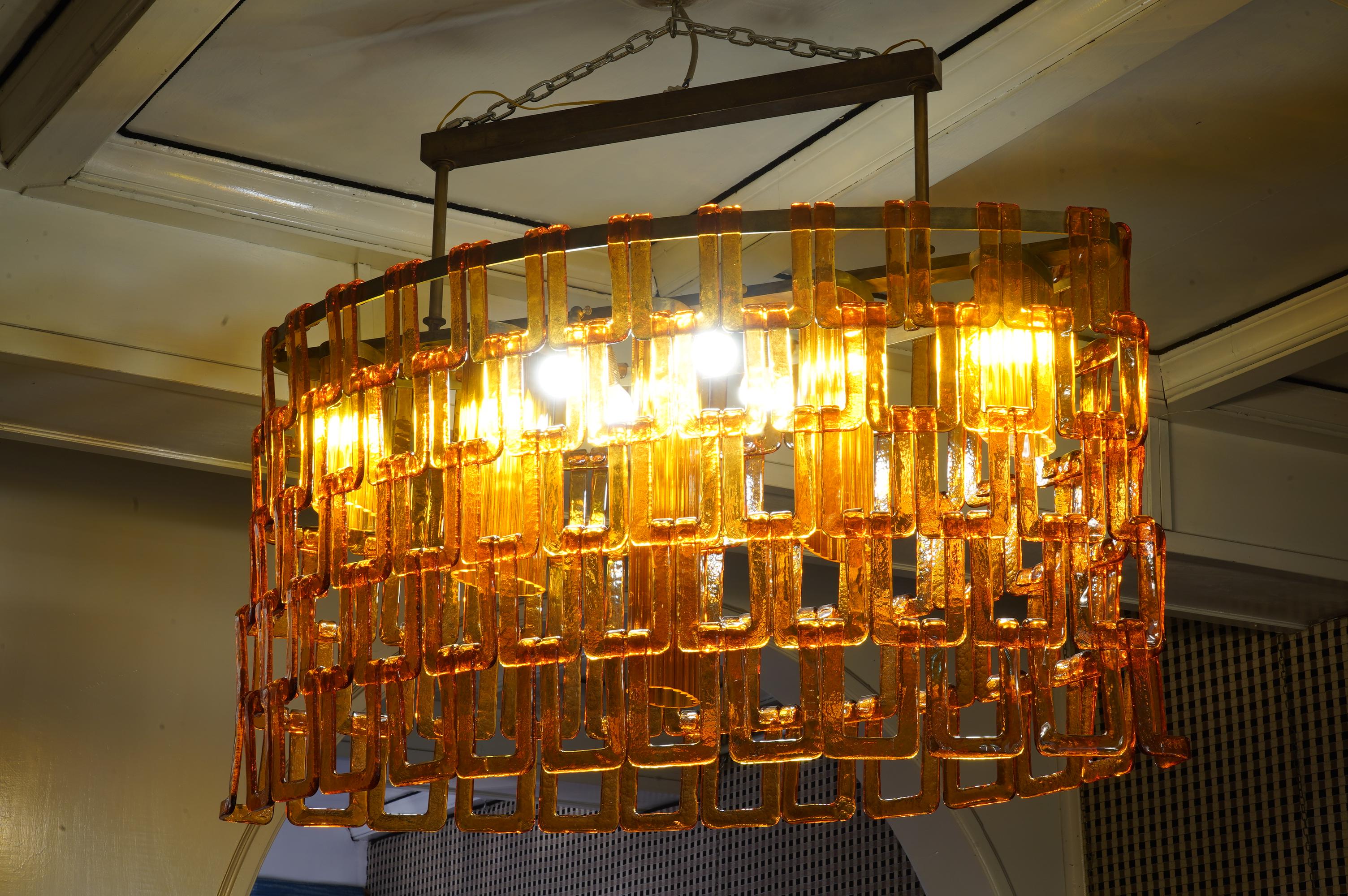 Simple and precious chandelier in Murano orange glass, from the furnace of Vistosi. Its oval design is very elegant.

The chandelier consists of a brass frame and its oval design. All around have been hung some 
