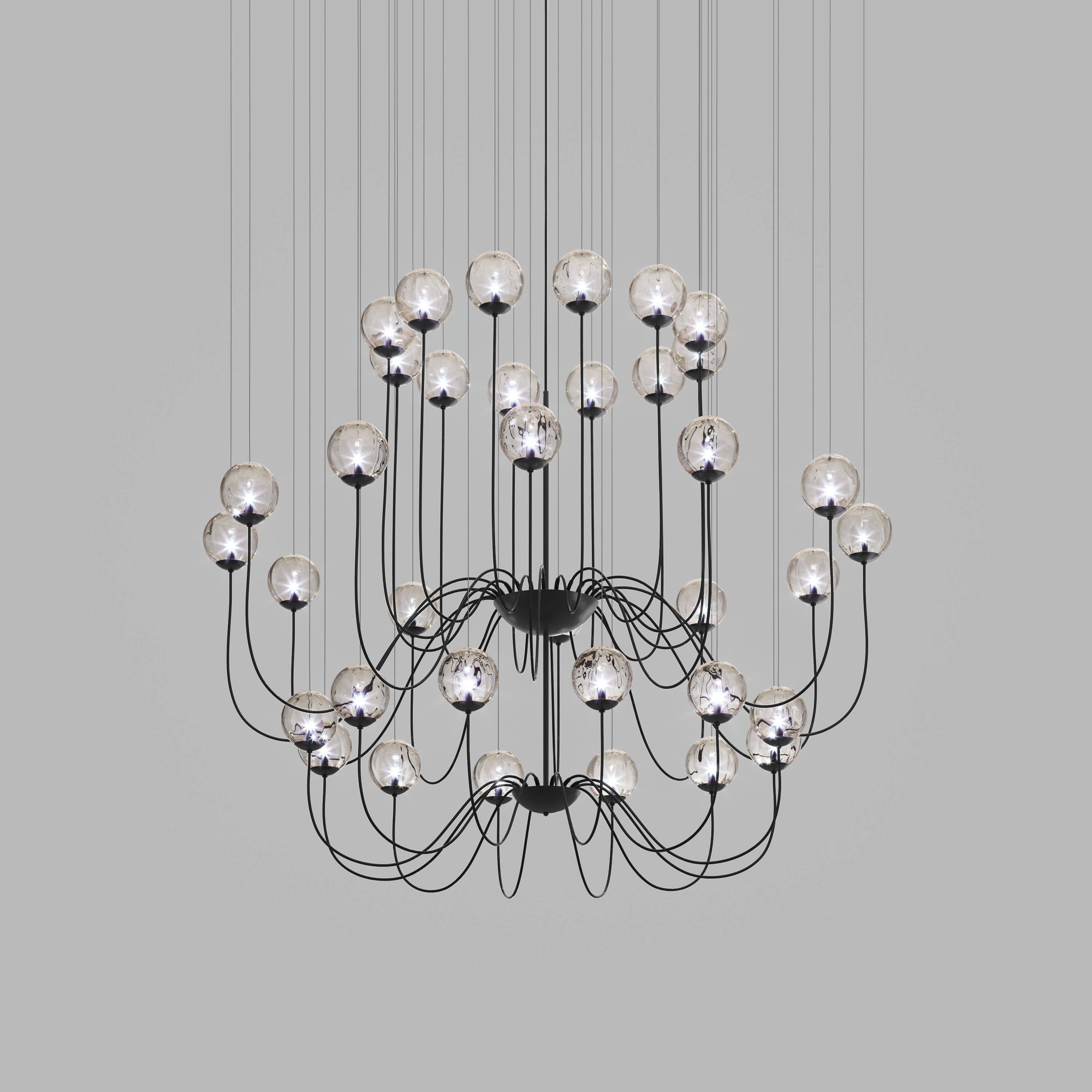 Collezione di lampade con diffusore in vetro soffiato e irregolare a righe. Le tre dimensioni delle sfere e le diverse altezze dei cavi sono pensate per creare composizioni eleganti. La versione lampadario permette di fissare i diffusori con cavi