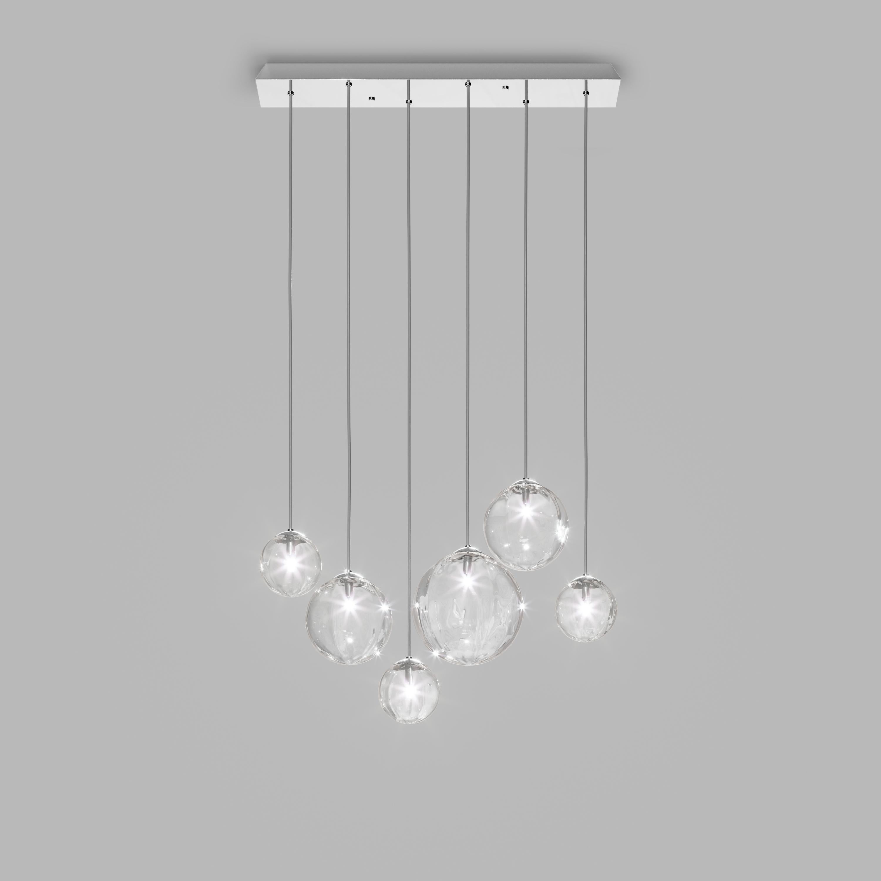 Collezione di lampade con diffusore in vetro soffiato e irregolare a righe. Le tre dimensioni delle sfere e le diverse altezze dei cavi sono pensate per creare composizioni eleganti. La versione lampadario permette di fissare i diffusori con cavi