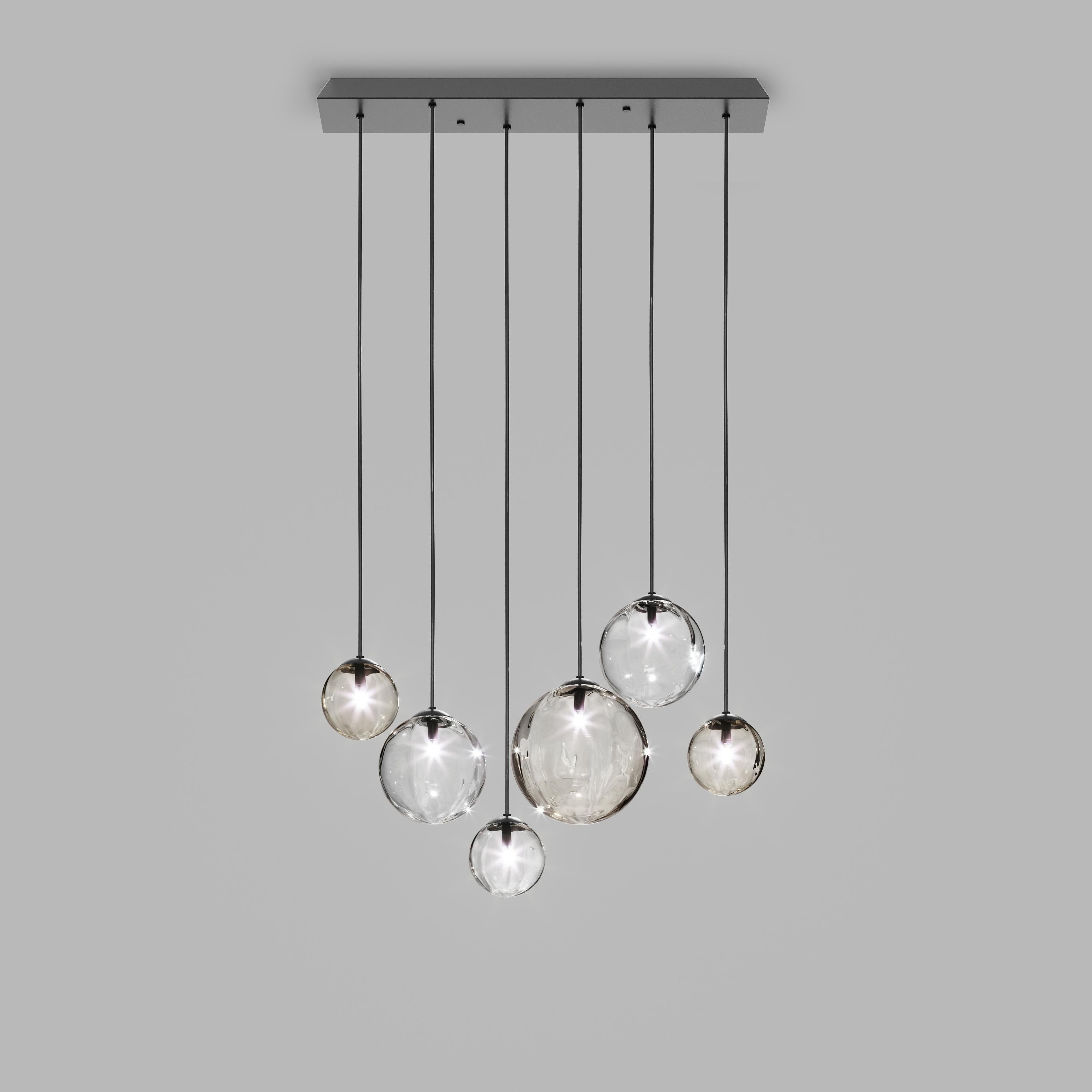 Collezione di lampade con diffusore in vetro soffiato e irregolare a righe. Le tre dimensioni delle sfere e le diverse altezze dei cavi sono pensate per creare composizioni eleganti. La versione lampadario permette di fissare i diffusori con cavi