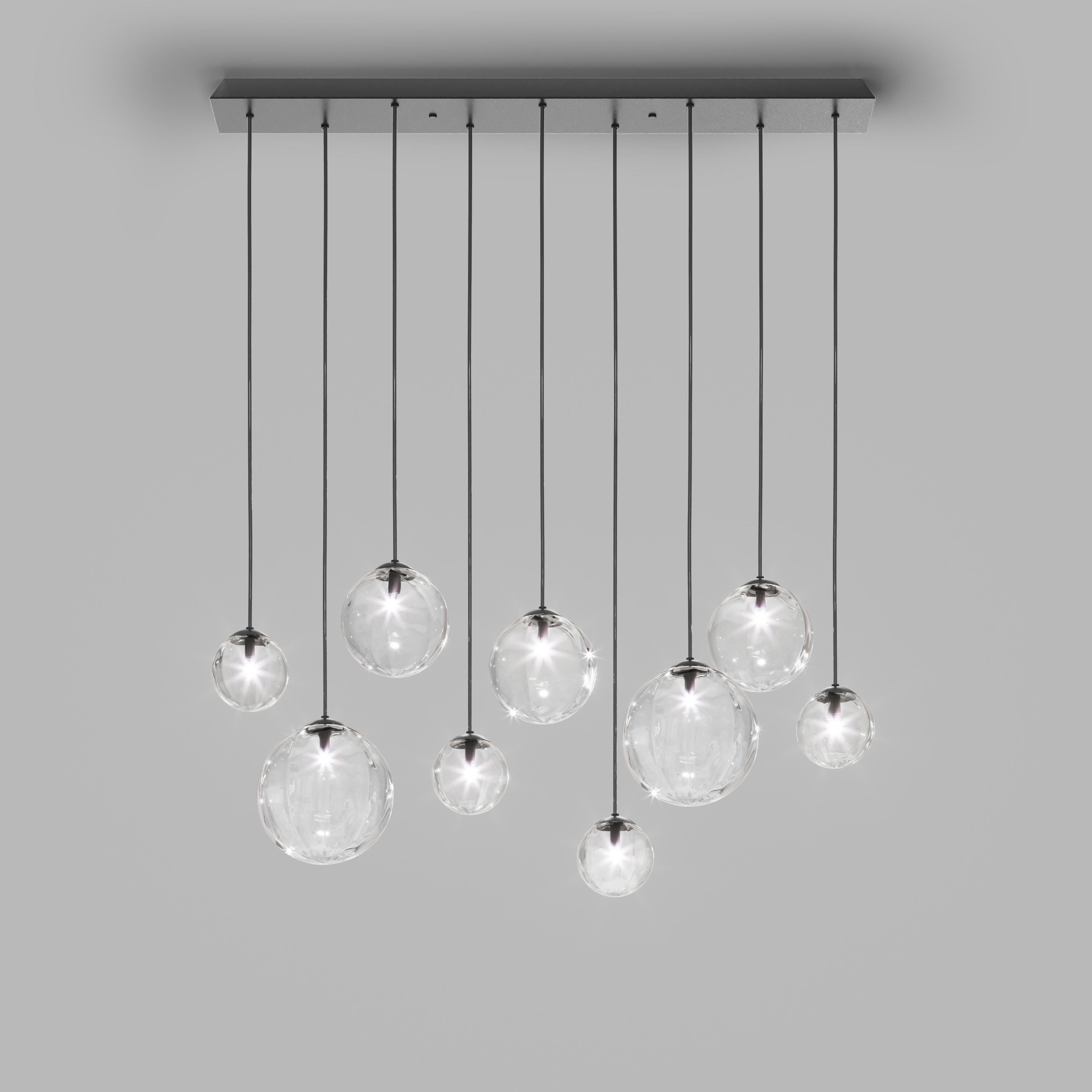 Collection of lamps with a blown and irregular striped glass diffuser. The three sizes of the spheres and the different cable heights are designed to create elegant compositions. The chandelier version allows to fix the diffusers with steel cables