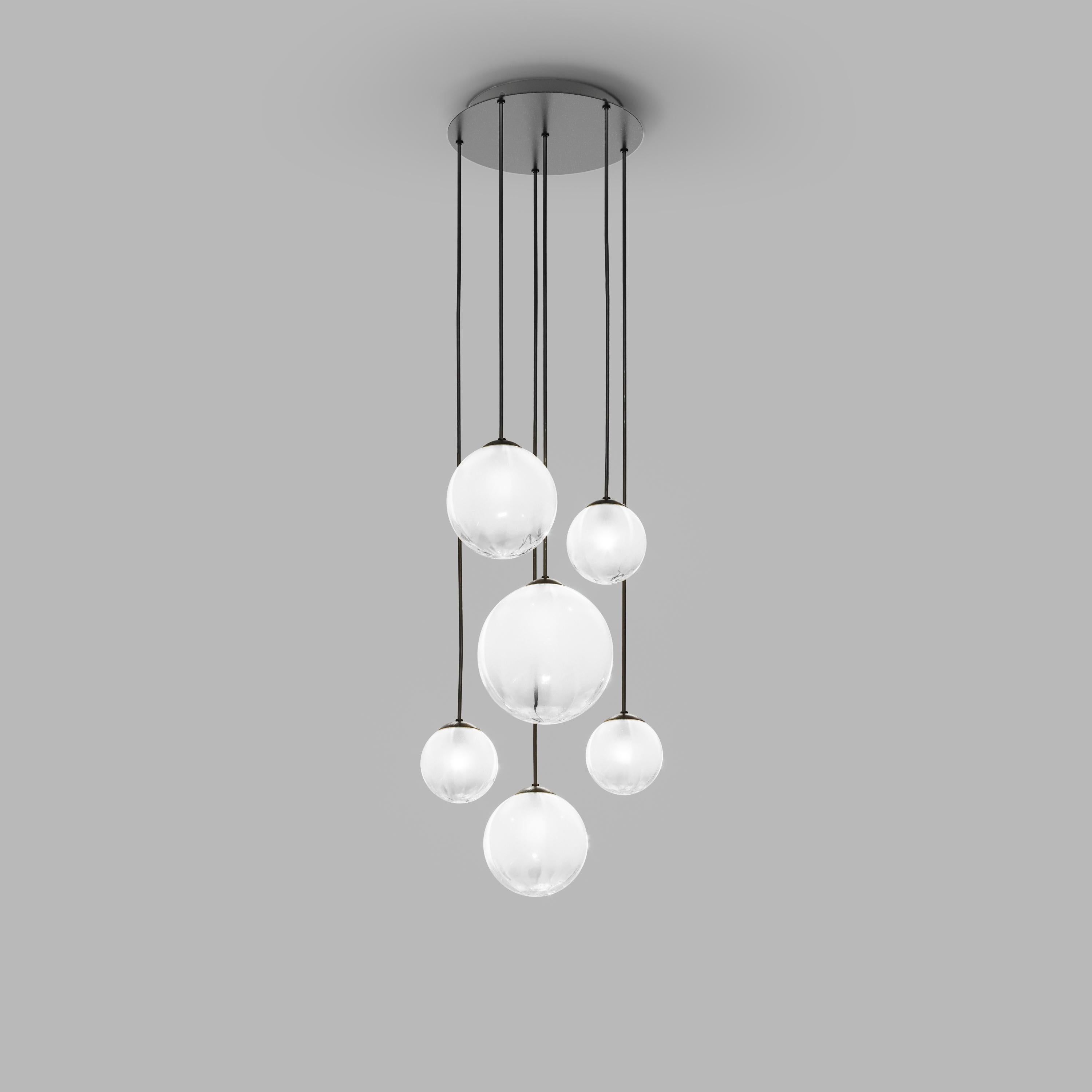 Collezione di lampade con diffusore in vetro soffiato e irregolare a righe. Le tre dimensioni delle sfere e le diverse altezze dei cavi sono pensate per creare composizioni eleganti. La versione lampadario permette di fissare i diffusori con cavi