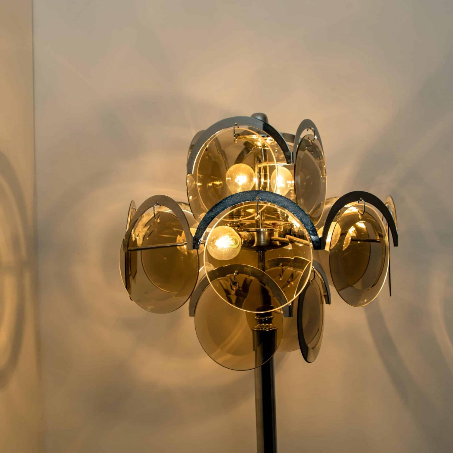 Una splendida lampada da terra con dischi in vetro fumé, asta centrale cromata e base circolare cromata, nello stile di Gino Vistosi.

Buone condizioni d'epoca con pochi segni d'uso commisurati all'età. I dischi di vetro sono in perfette