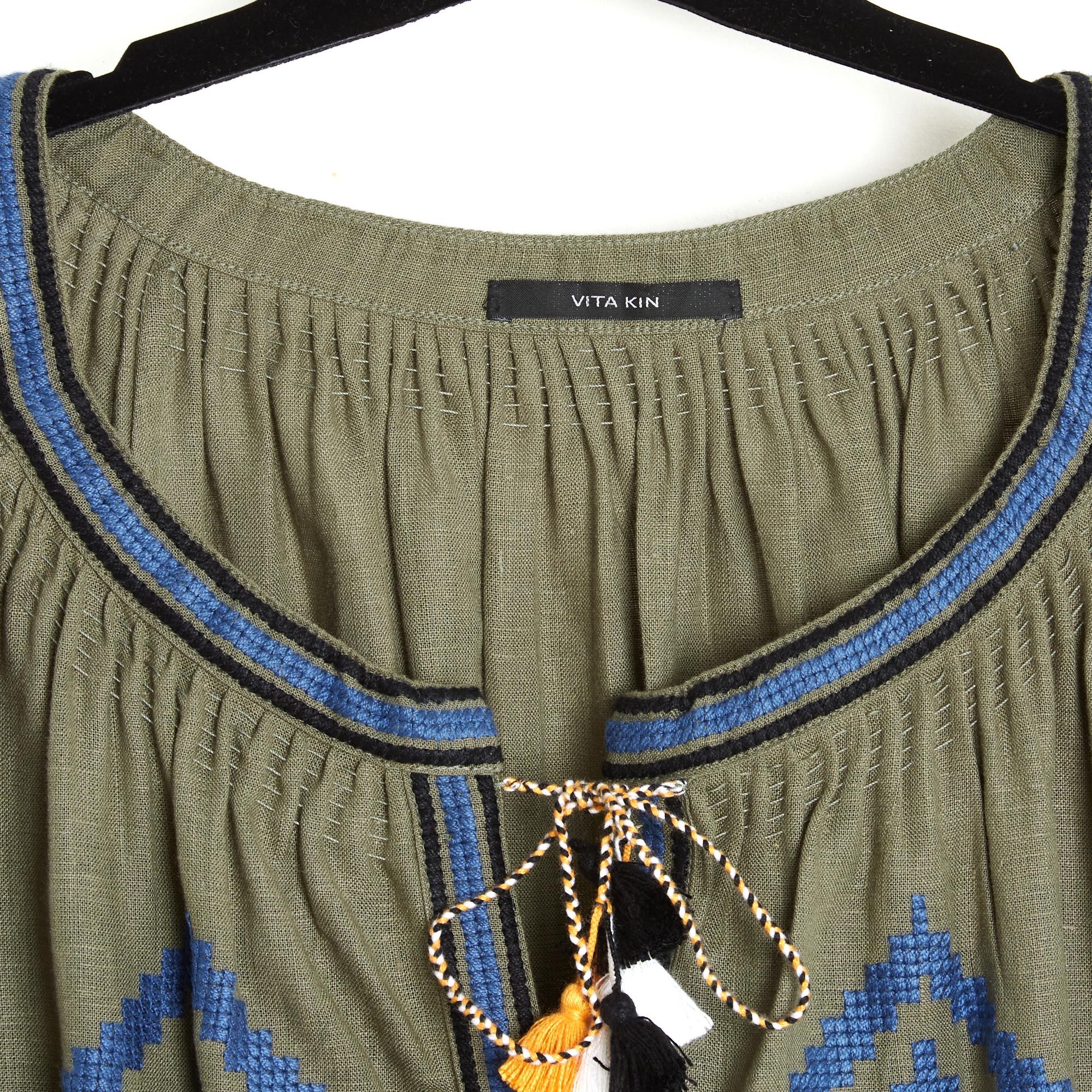 Vita Kin dress in linen embroidered with ethnic-inspired patterns (Ukraine) in different colored threads, wide round neck closed by ties and multicolored pompoms up to the waist, then by hidden snaps to the bottom, black fabric inserts and slit