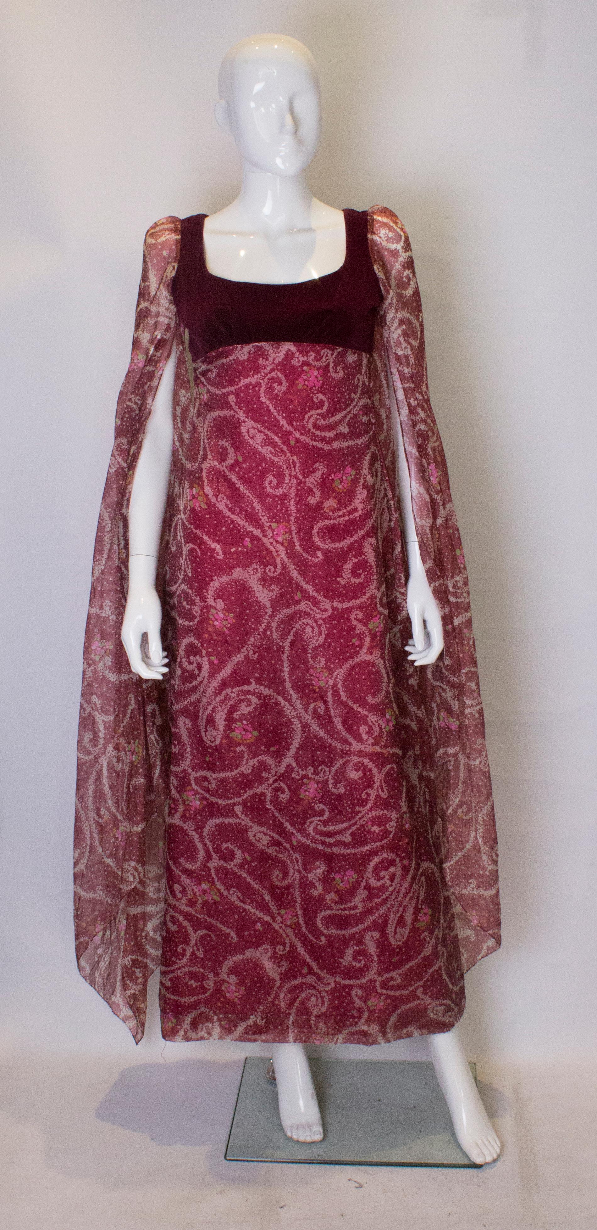 A stunning gown by British design house Quad. The gown has a burgundy velvet bust area with wonderful long open sleaves in a burgundy, pink, green and ivory print. This print is also on the body of the dress. The gown is fully lined and a has a
