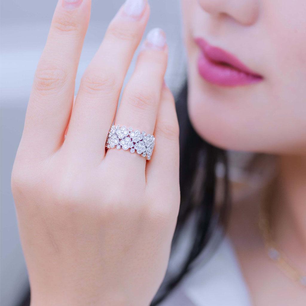 Cette élégante bague à large bande en or blanc 18 carats présente un motif floral complexe composé de diamants ronds de taille brillant totalisant environ 3,34 carats. Chaque fleur est délicatement encadrée de fins détails de milgrain, ajoutant une