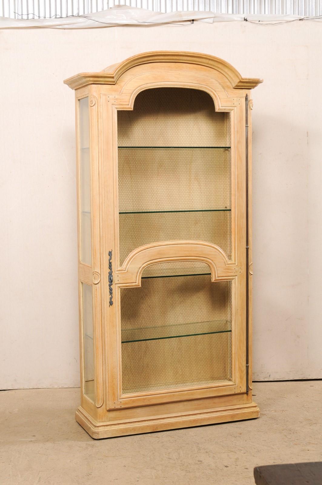 A vintage American carved-wood tall cabinet with glass display shelves. This vitrine cabinet features a nicely molded arch pediment at top, with single front door mimicking the arch at top, flanked within rounded wooden side posts, and glass panel