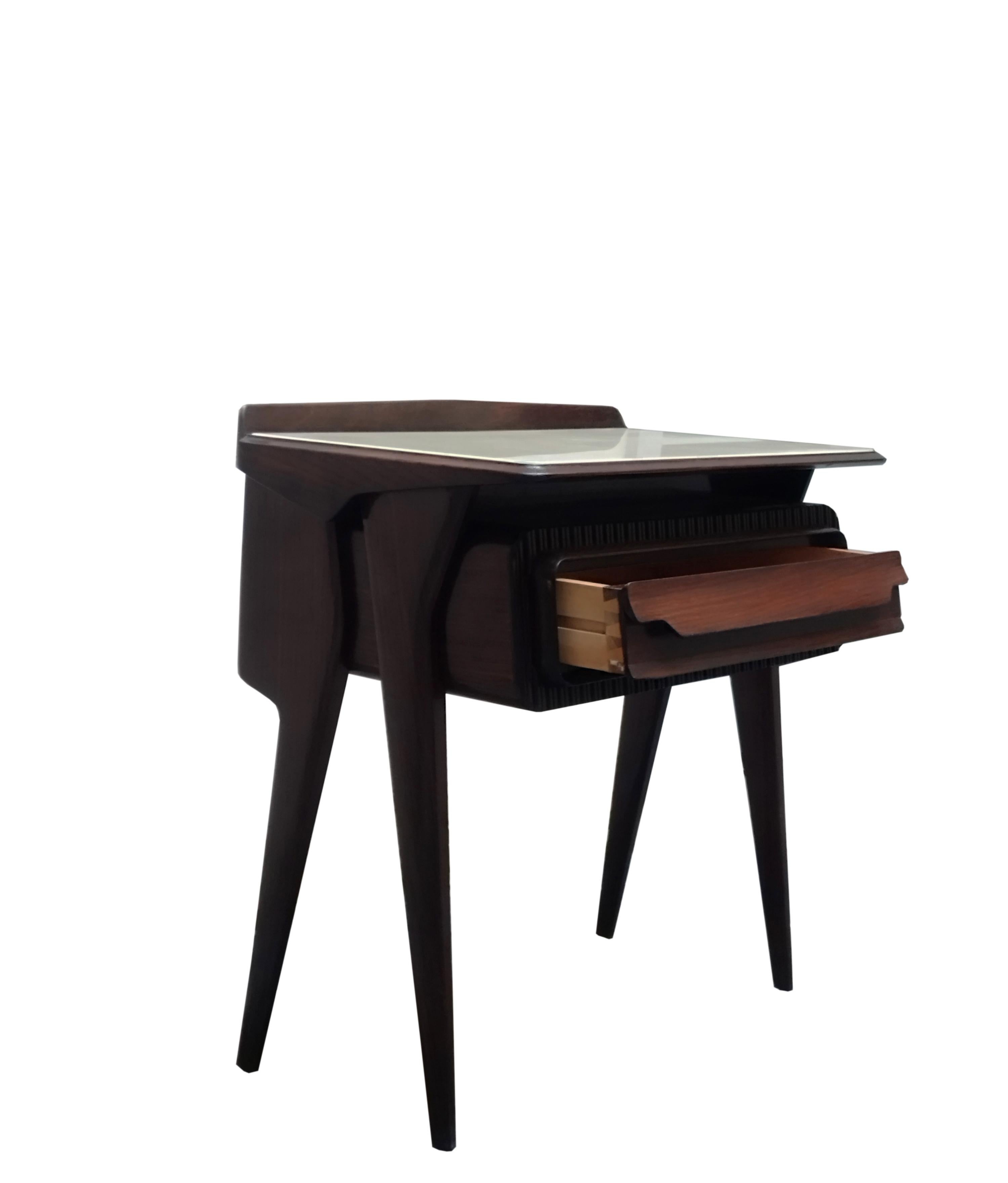 Nachttisch aus Holz, entworfen von Vittorio Dassi in den 1950er Jahren.
 Seine ästhetische Einzigartigkeit liegt in der originellen skulpturalen Gestaltung der Form der Schublade und der seitlichen Stützen sowie der Glasplatte. Wirklich in