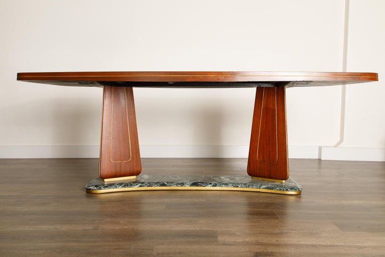 This gorgeous sculptural mahogany dining table by Vittorio Dassi is a magnificent example of 1950s Italian Modernism. Sculpted from precious mahogany wood, Fine green colored glass, green marble, and brass inlays and trim. 

This incredible