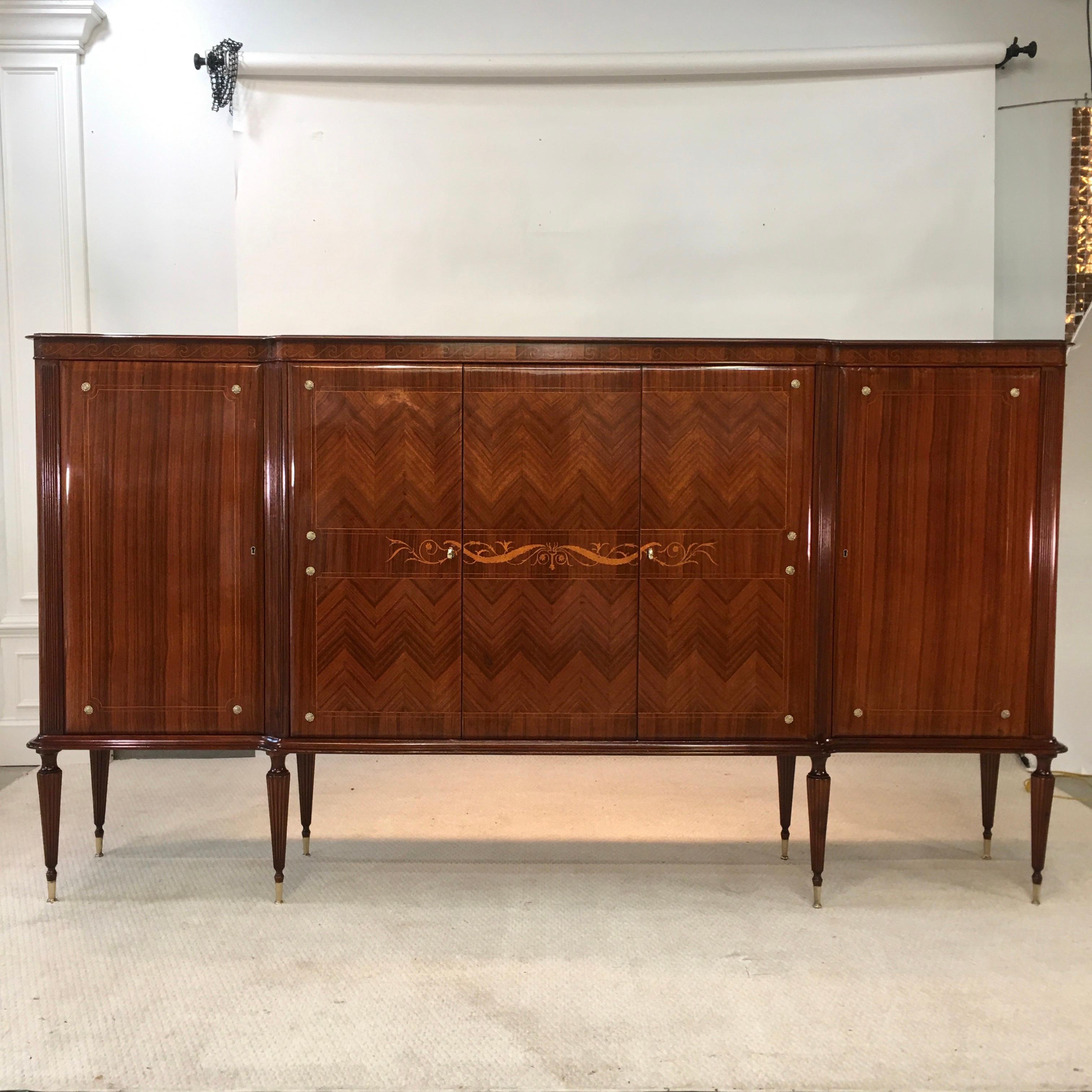 1950s Italian extra large sideboard bar cabinet by Vittorio Dassi in beautifully executed herringbone pattern rosewood and mahogany supported on eight tapered and fluted legs with brass sabots.
Distinctive intarsia border in Italian deco motif of