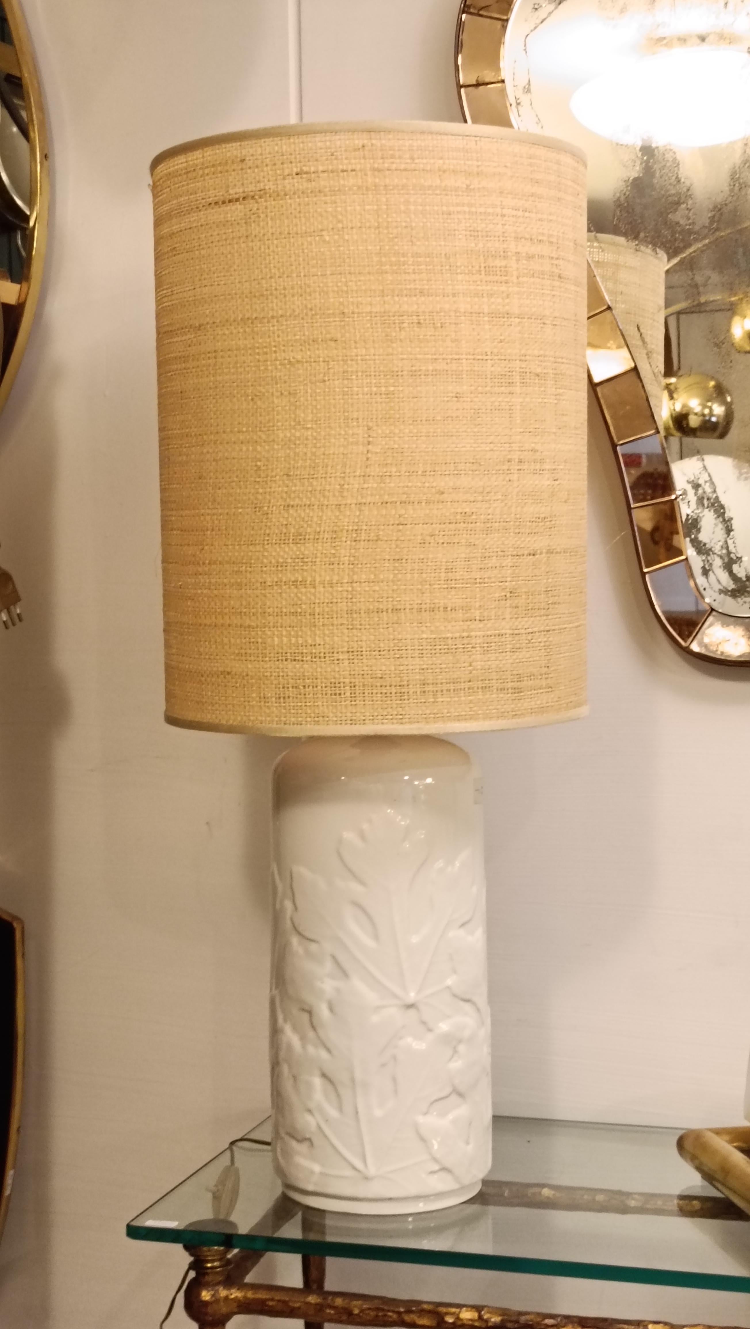 White ceramic table lamp, cylindrical in shape, features a delicate raised leaf pattern that adds texture and a unique decorative touch.
The fabric shade, in a neutral, natural color, diffuses a soft, welcoming light, perfect for illuminating a