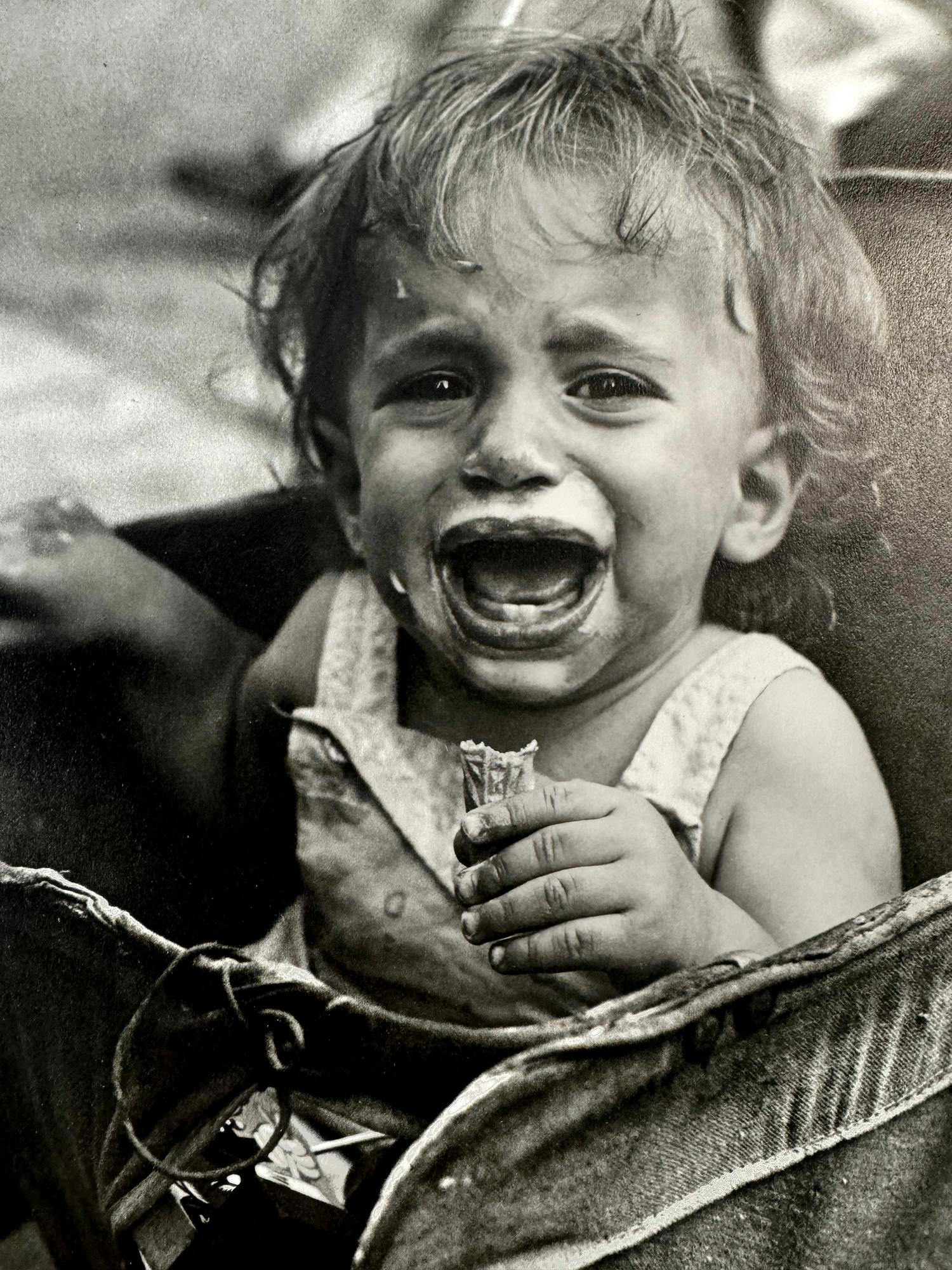 Female Street Photographer Vivian Maier captures a riveting moment of a child consumed in grief. The physiological and psychological anguish dominates her young face with arch eyes and a stressed, wide open mouth. The image personifies childhood