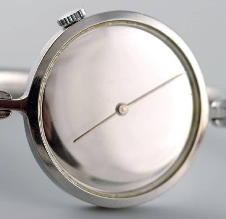 Vivianna Torun Bülow-Hübe for Georg Jensen: 
A lady's bangle wristwatch of steel. 
Design no. 227. Mechanical movement with manual winding. 1970's.
Mirror dial with silvered hands. Integrated bangle bracelet of steel. Circumference app. 16 cm. Watch