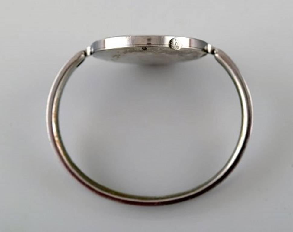Vivianna Torun Bülow-Hübe for Georg Jensen: 
A lady's bangle wristwatch of steel. 
Design no. 227. Mechanical movement with manual winding. 1970's.
Mirror dial with silvered hands. Integrated bangle bracelet of steel. Circumference app. 16 cm. Watch