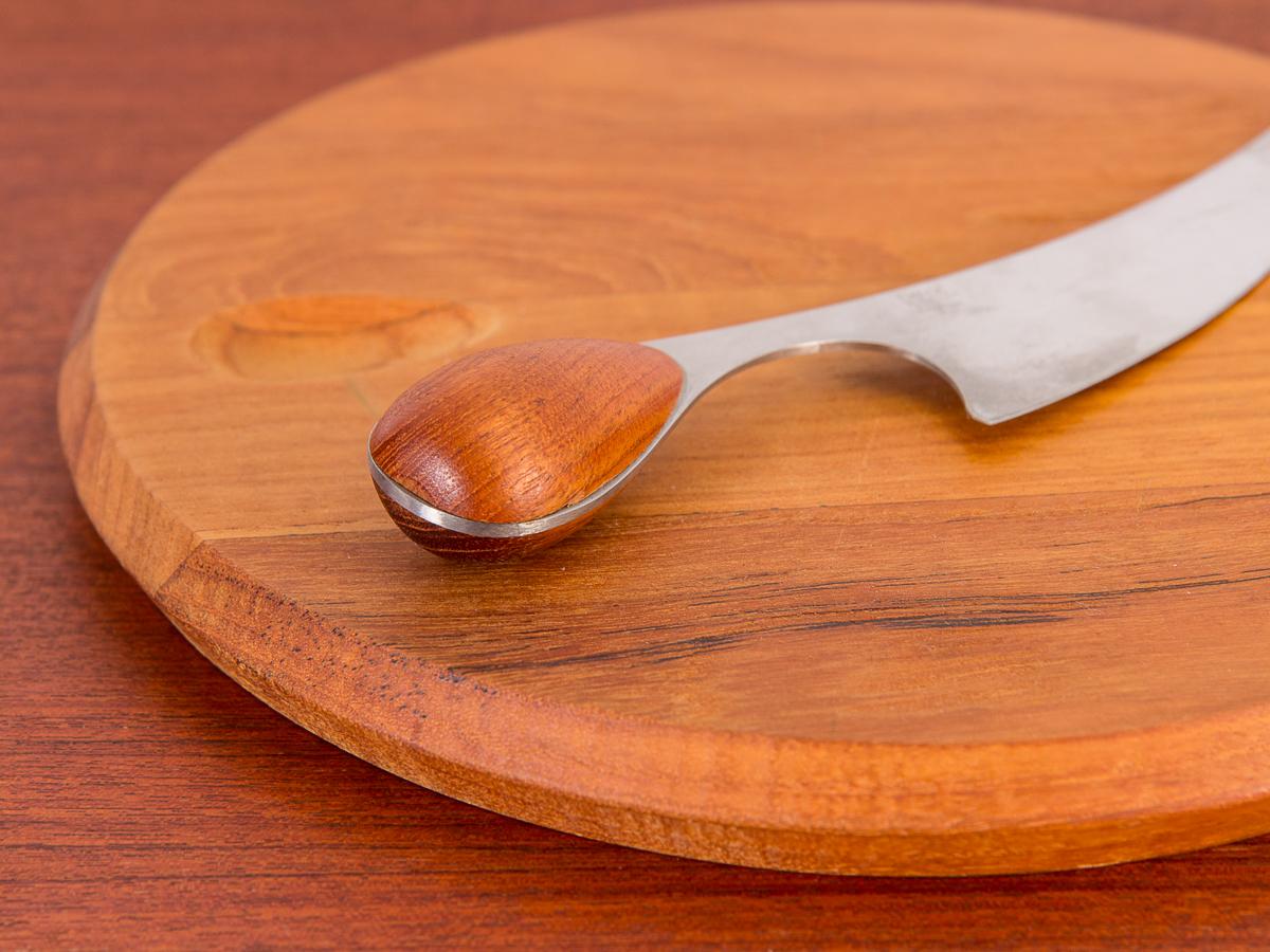 Gorgeous circular teak cheeseboard with knife designed by master jeweler and silversmith Vivianna Torun Bulow-Hube for Dansk. An impressive serving piece for cheese and charcuterie, complete with a stainless steel knife. A carved slot cradles the