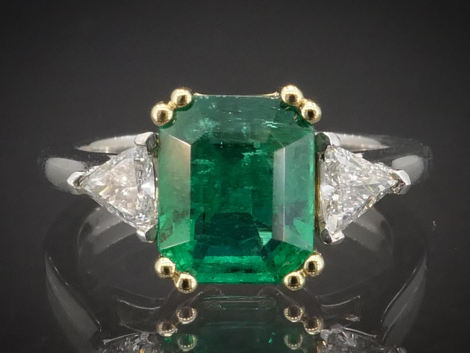 Beautiful two tone mounting made from platinum and 18k yellow gold. Newly mounted 1.88ct (8.6mm by 7.1mm ) Zambian Emerald set in the middle with .31ctw of trillion cut diamond accents. SI1 clarity with HI color. Unique combo and cut to the stones