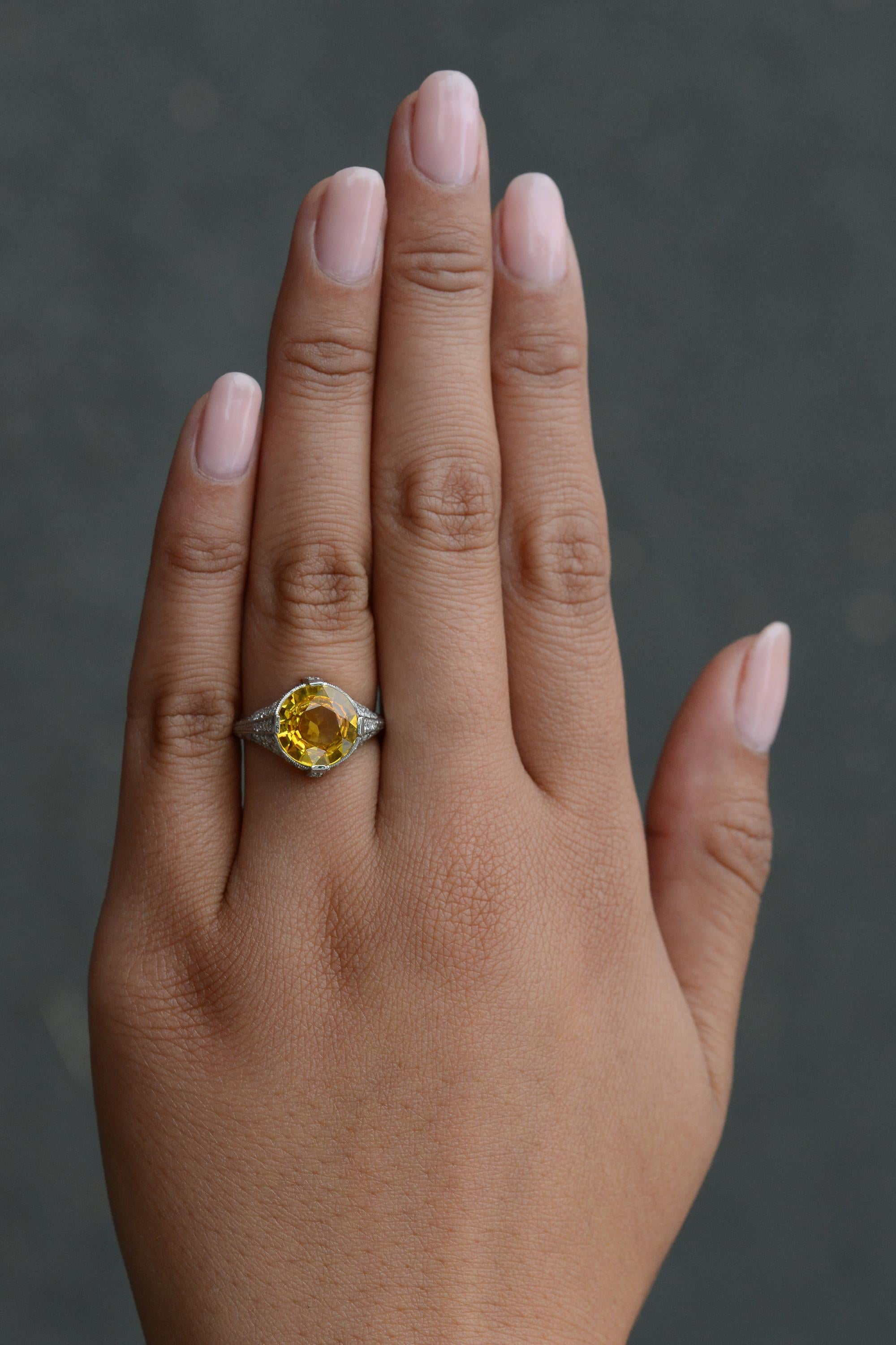 This vibrant ring surely adds a drop of sunshine to your hand! Centered on a vivid, 4 carat flaming yellow sapphire which makes for an incredibly striking gemstone engagement ring. The setting is an authentic 1920s Jazz Age Art Deco masterpiece